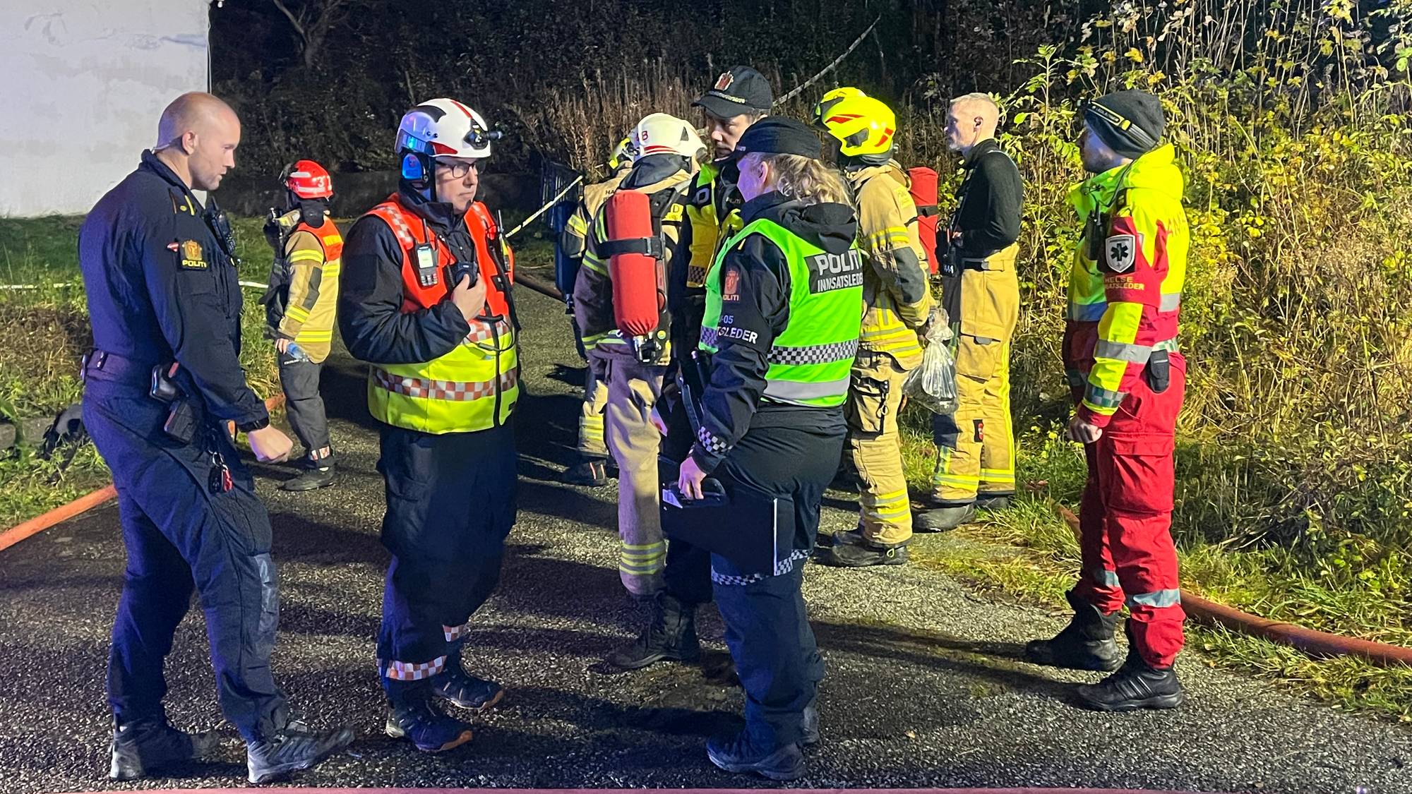 Politi, brannvesen og ambulansepersonell samlet på et skadested om natten. (Bildebeskrivelsen er laget av en KI-tjeneste)