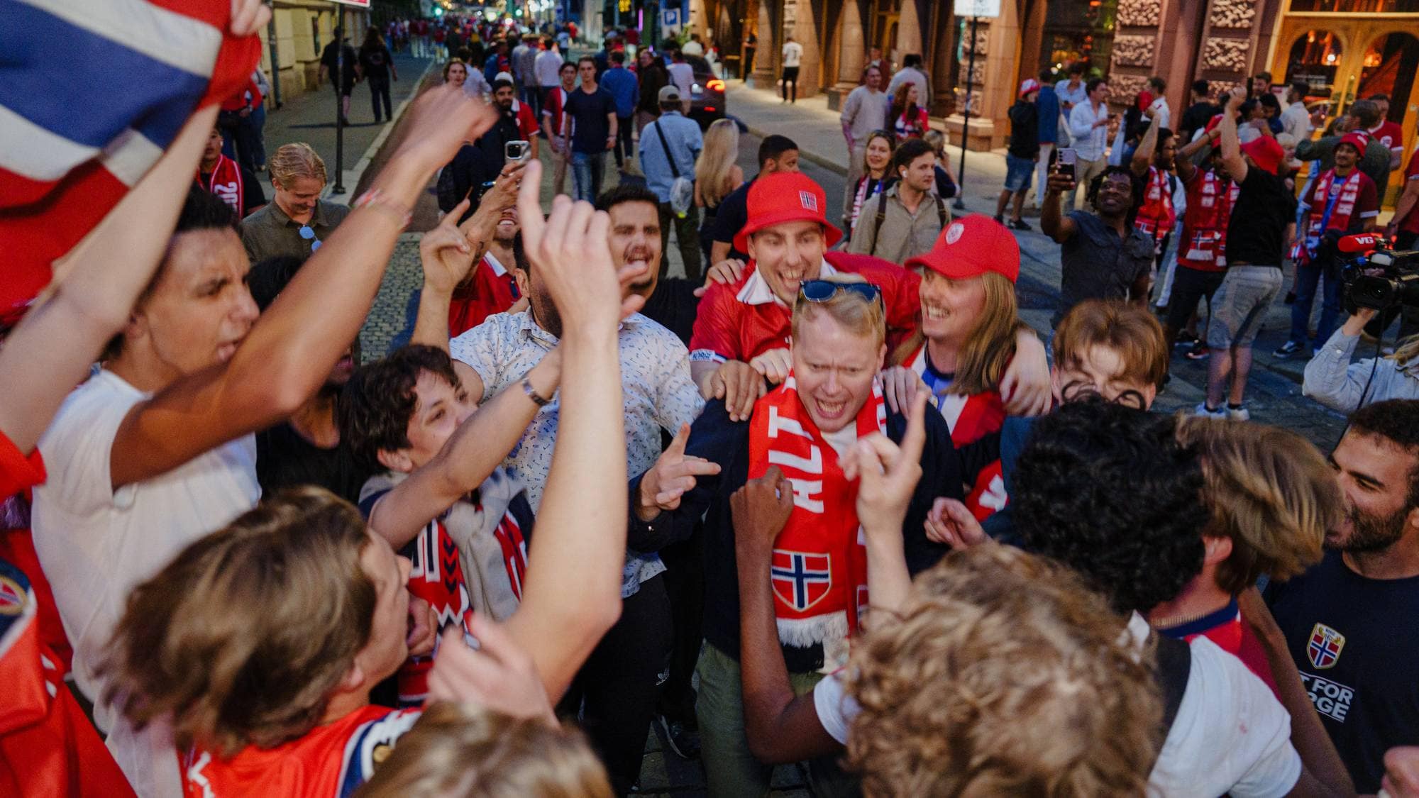 Folkemengde i Oslos gater feirer med norske flagg og skjerf. Mange unge voksne jubler sammen ute. (Bildebeskrivelsen er laget av en KI-tjeneste)
