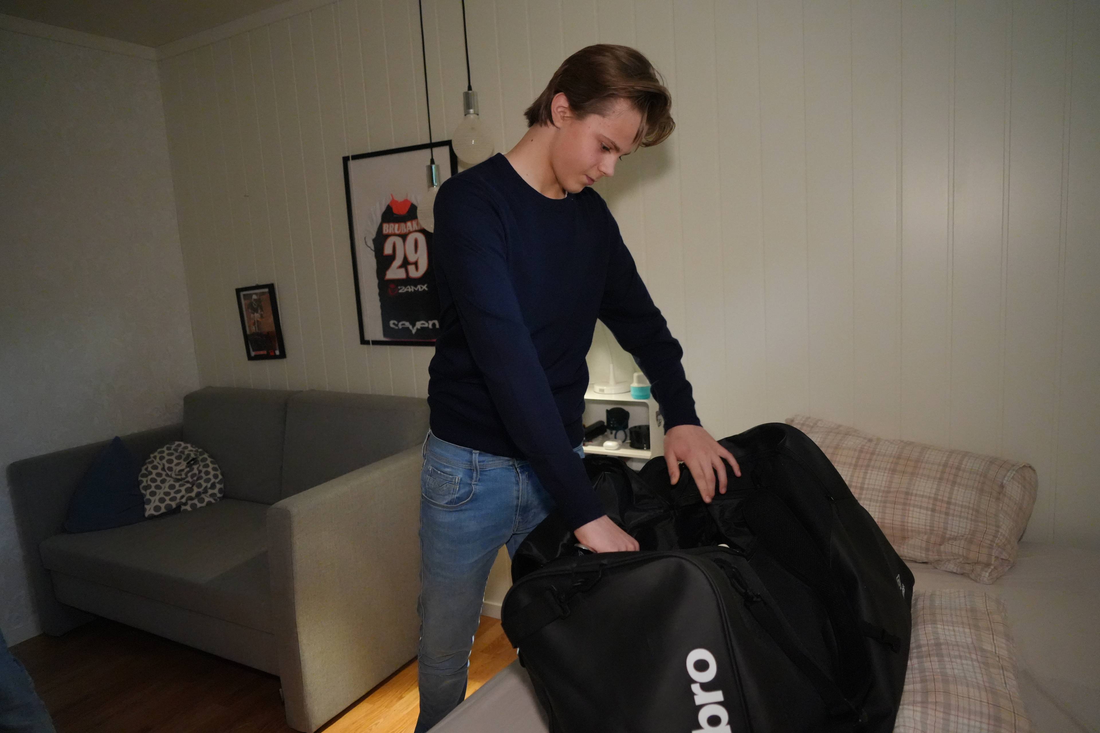 En ung mann står i et rom og pakker en svart treningsbag på en seng. (Bildebeskrivelsen er laget av en KI-tjeneste)