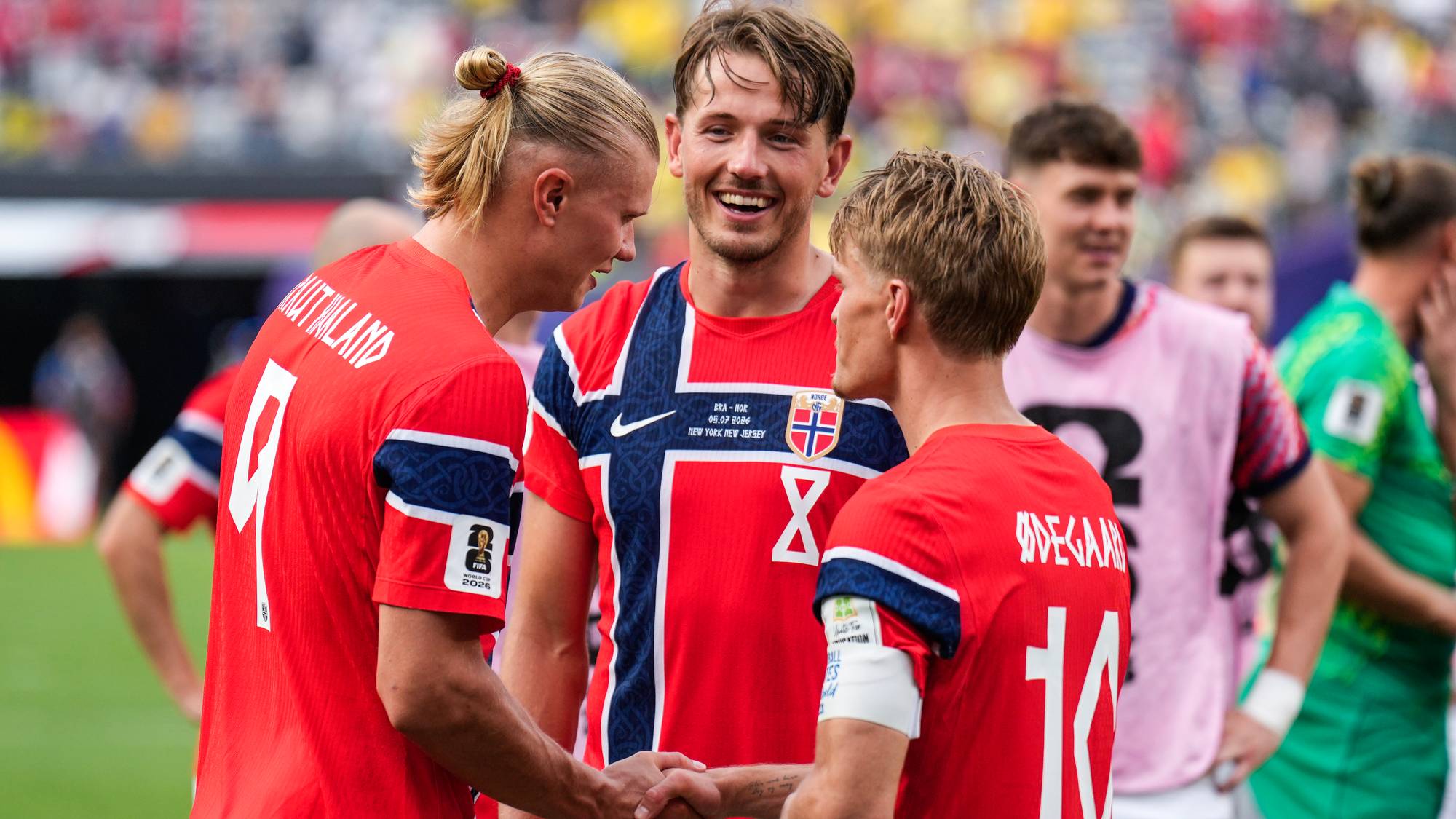 Erling Braut Haaland og Martin Ødegaard håndhilser på banen med en lagkamerat. (Bildebeskrivelsen er laget av en KI-tjeneste)