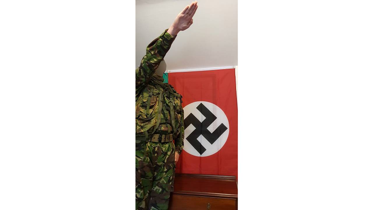 Ung britisk gutt i militærklær viser nazi-hilsen foran hakekors-flagg