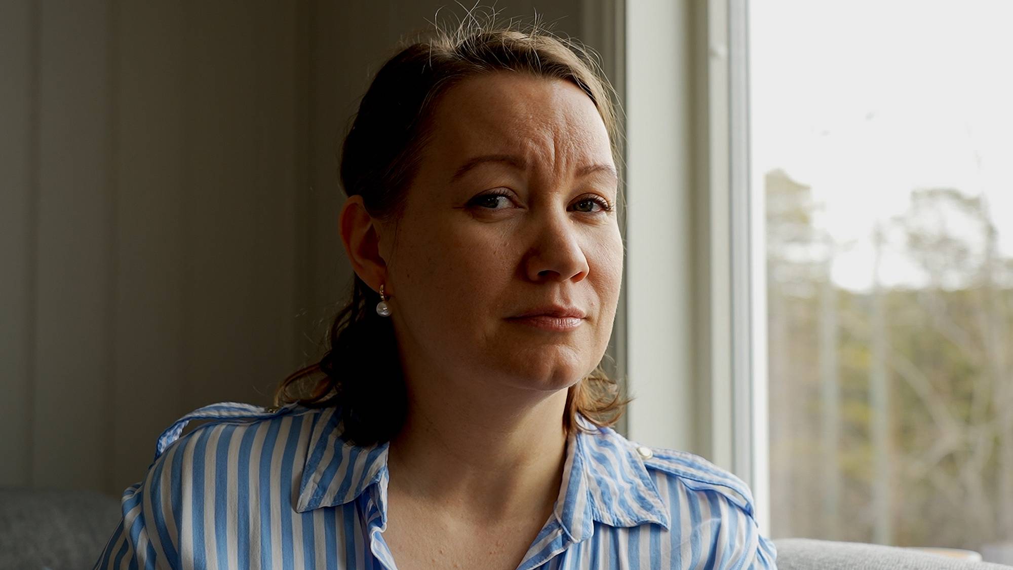 Kvinne som står ved vindu og ser inn i kamera