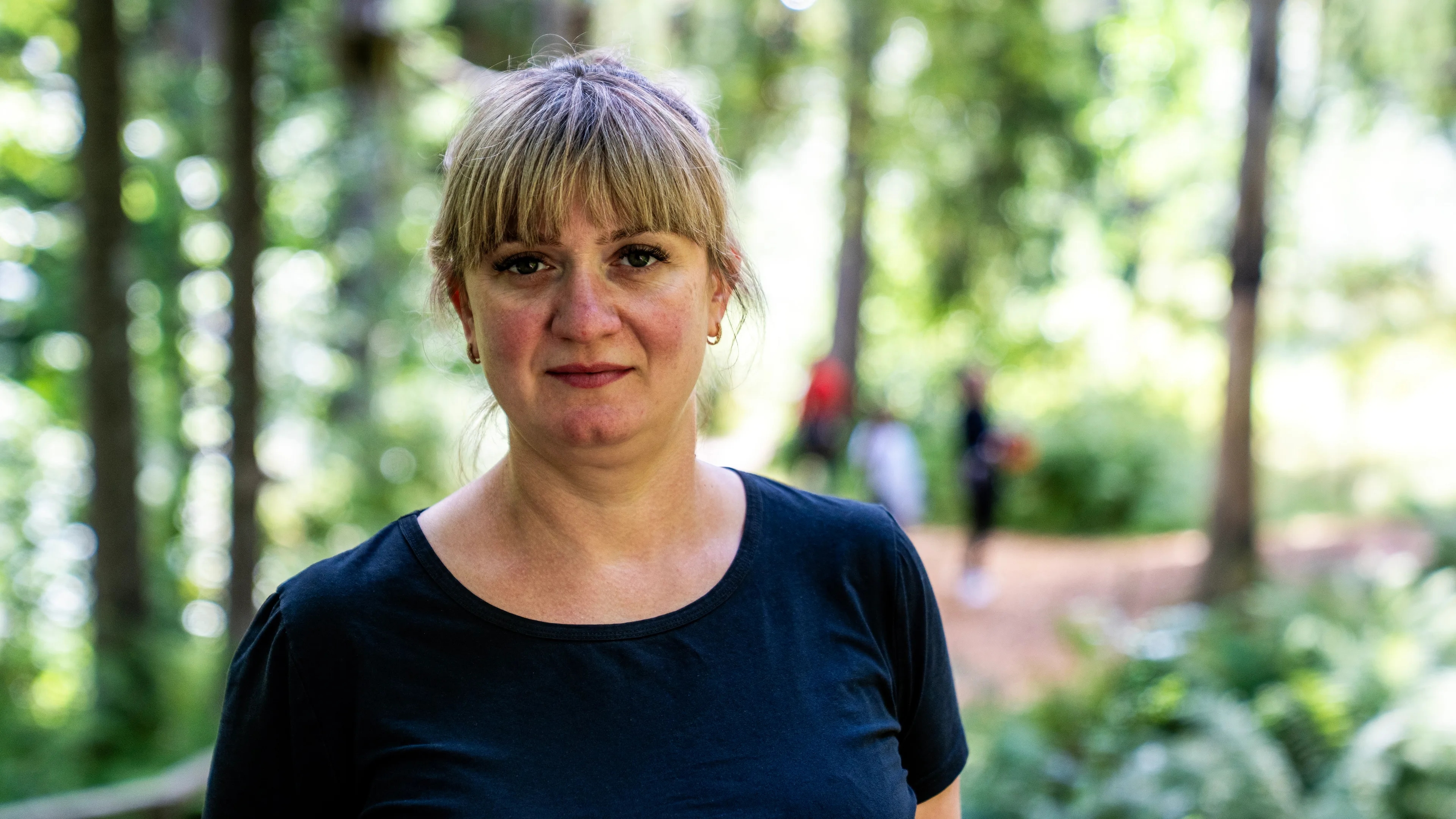 Portrett av ei alvorlig kvinne med håret i hestehale og sort T-skjorte. Klatrepark i bakgrunn