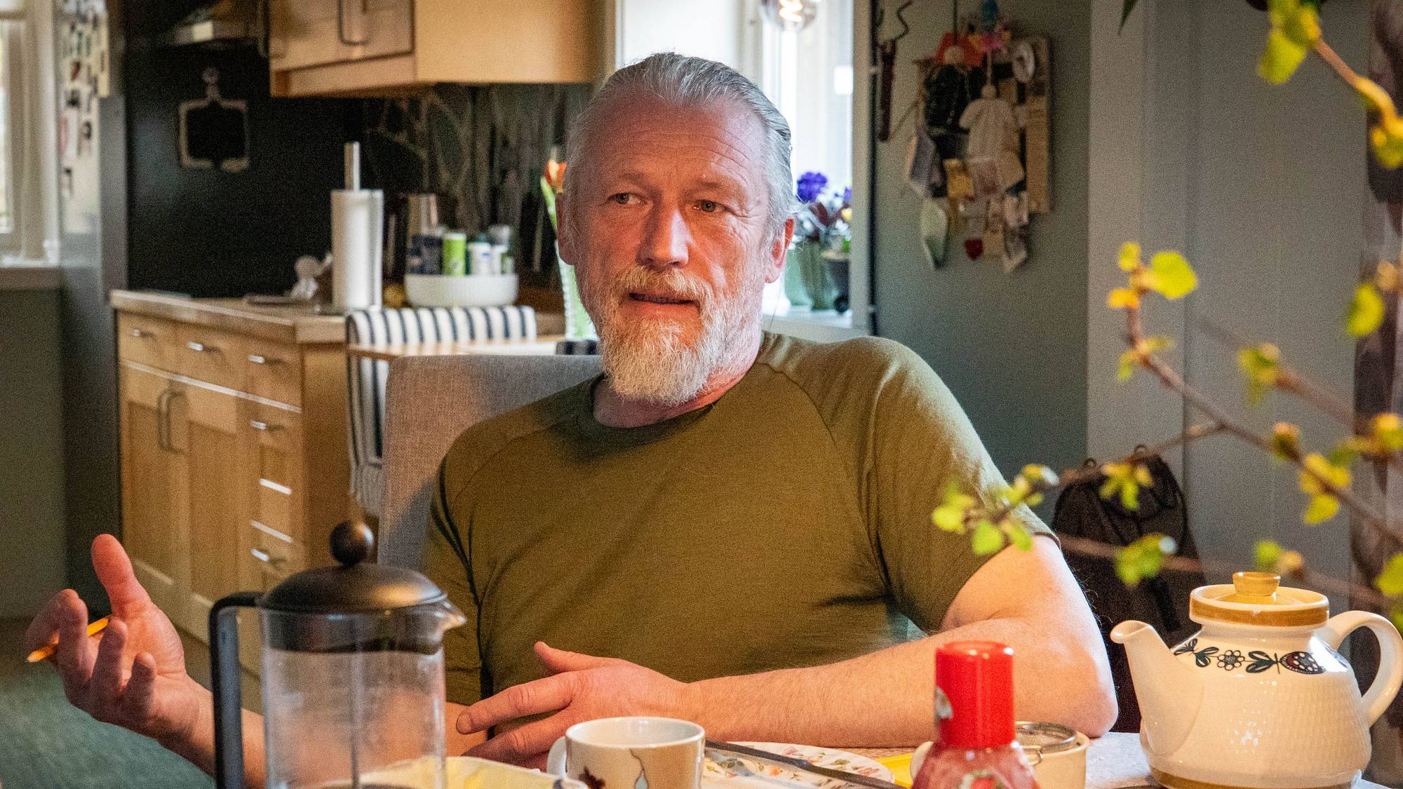 En mann med grått hår i hestehale og grønn t-skjorte sittende ved et bord