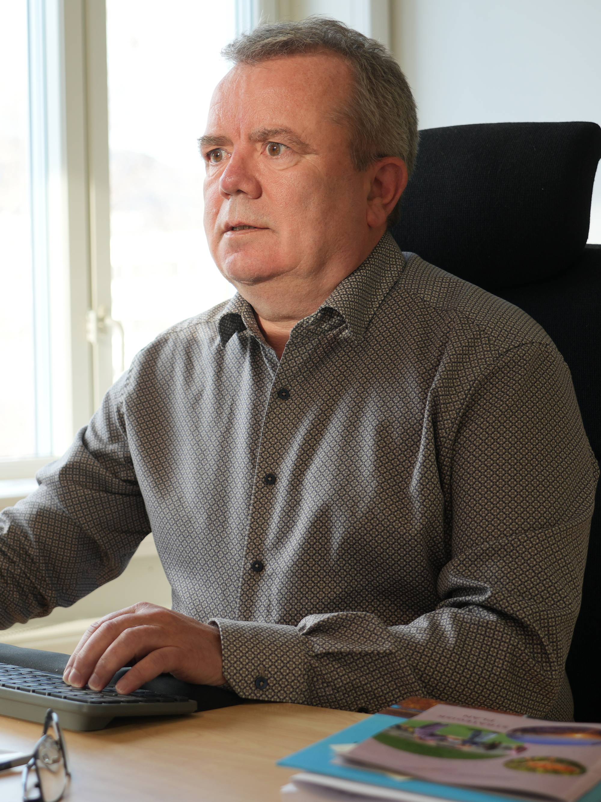 Mann sitter ved en pult på et kontor og jobber foran en dataskjerm. (Bildebeskrivelsen er laget av en KI-tjeneste)