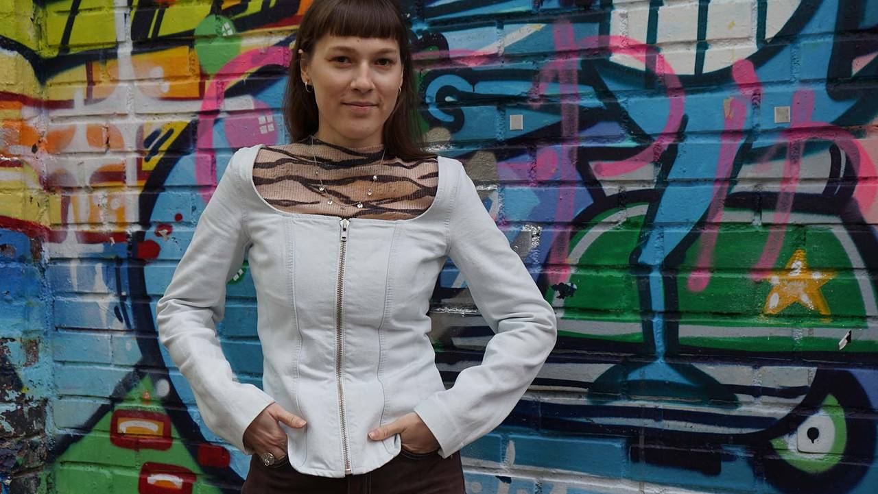 Katarina Barruk står foran en fargerik spraymalt vegg utenfor utestedet Blå i Oslo. På seg har hun en hvit jakke og brune bukser.