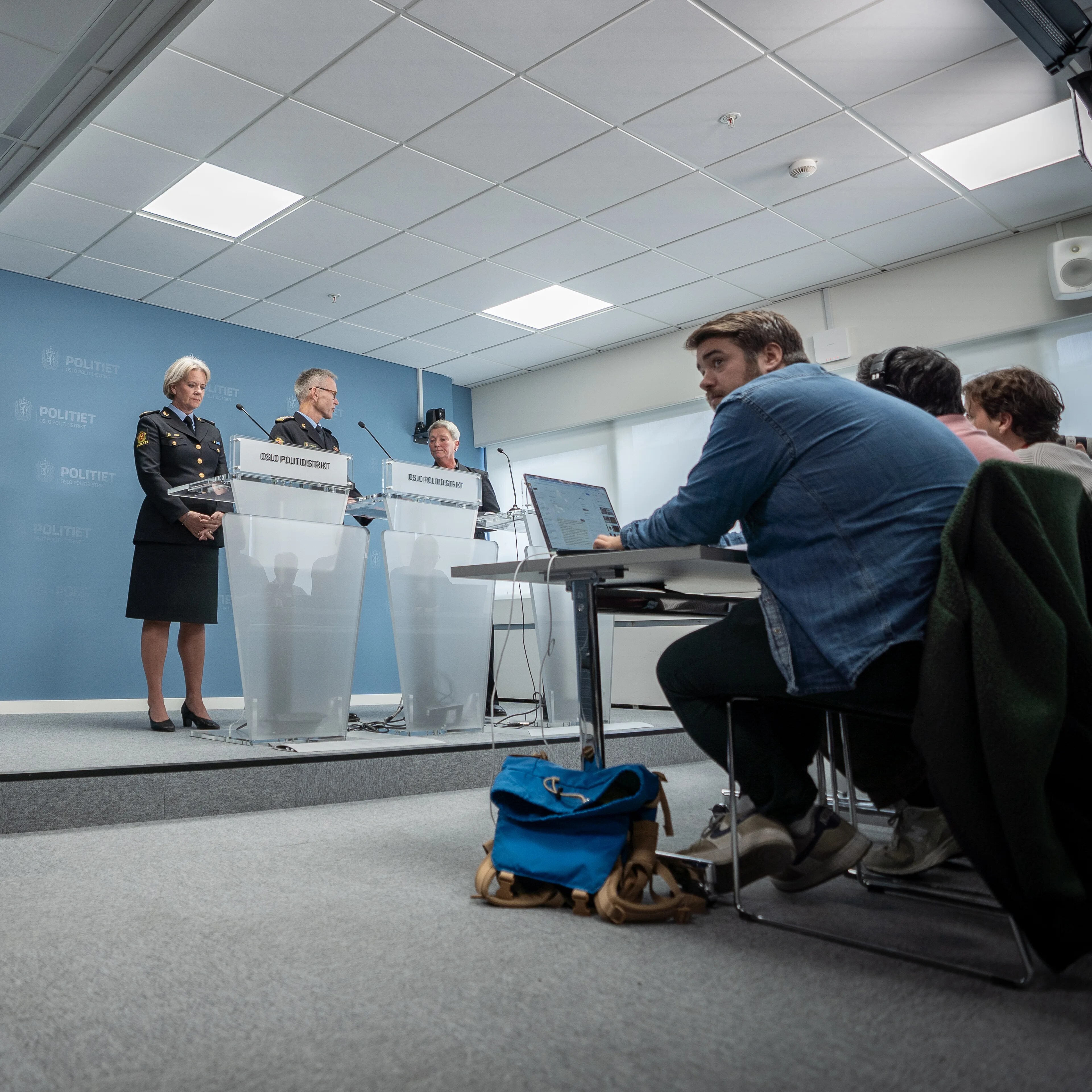 Politiets pressekonferanse med representanter bak talerstoler og journalister i rommet. (Bildebeskrivelsen er laget av en KI-tjeneste)