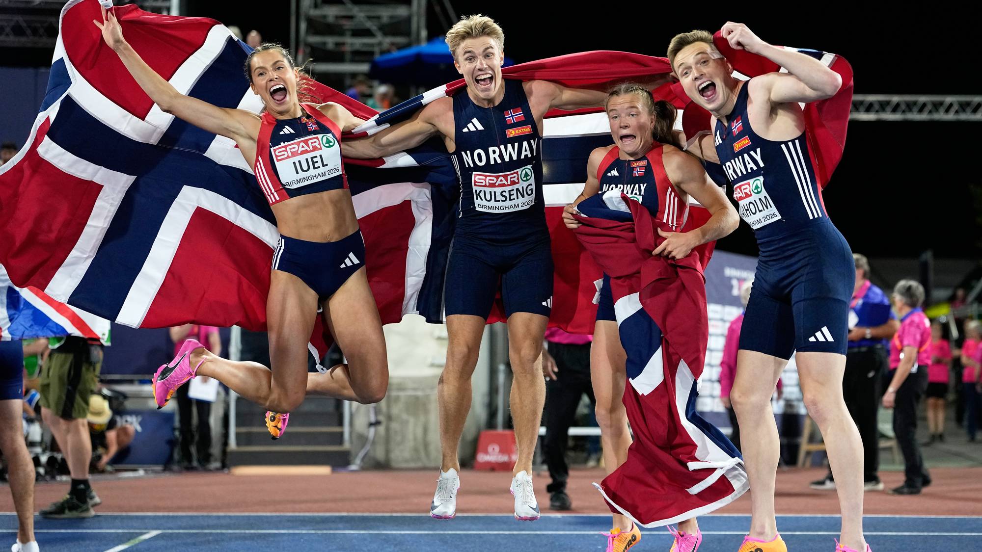 Norske friidrettsutøvere jubler med det norske flagget etter løp på en arena. (Bildebeskrivelsen er laget av en KI-tjeneste)