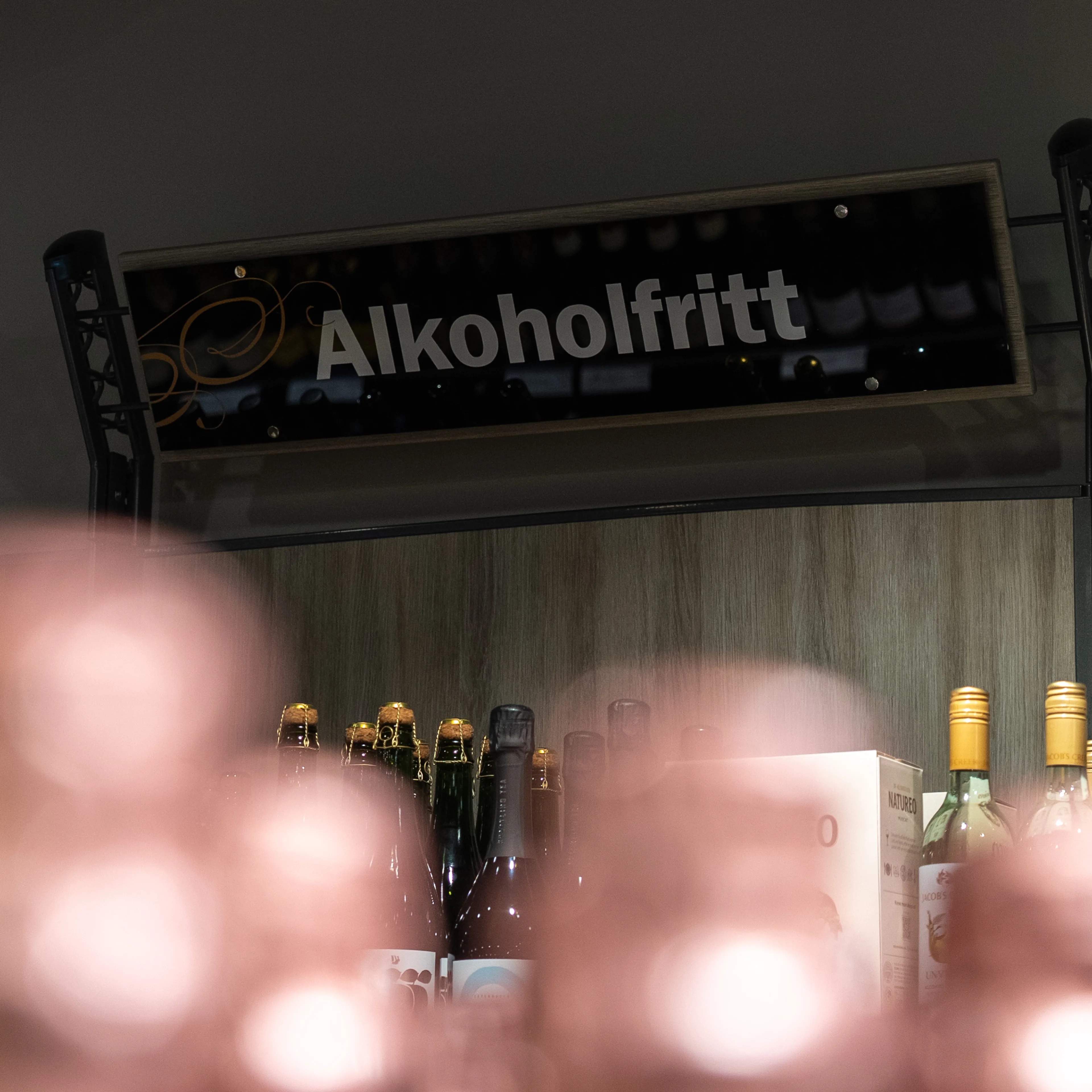 Skilt med teksten Alkoholfritt henger over en butikkhylle med ulike flasker. (Bildebeskrivelsen er laget av en KI-tjeneste)