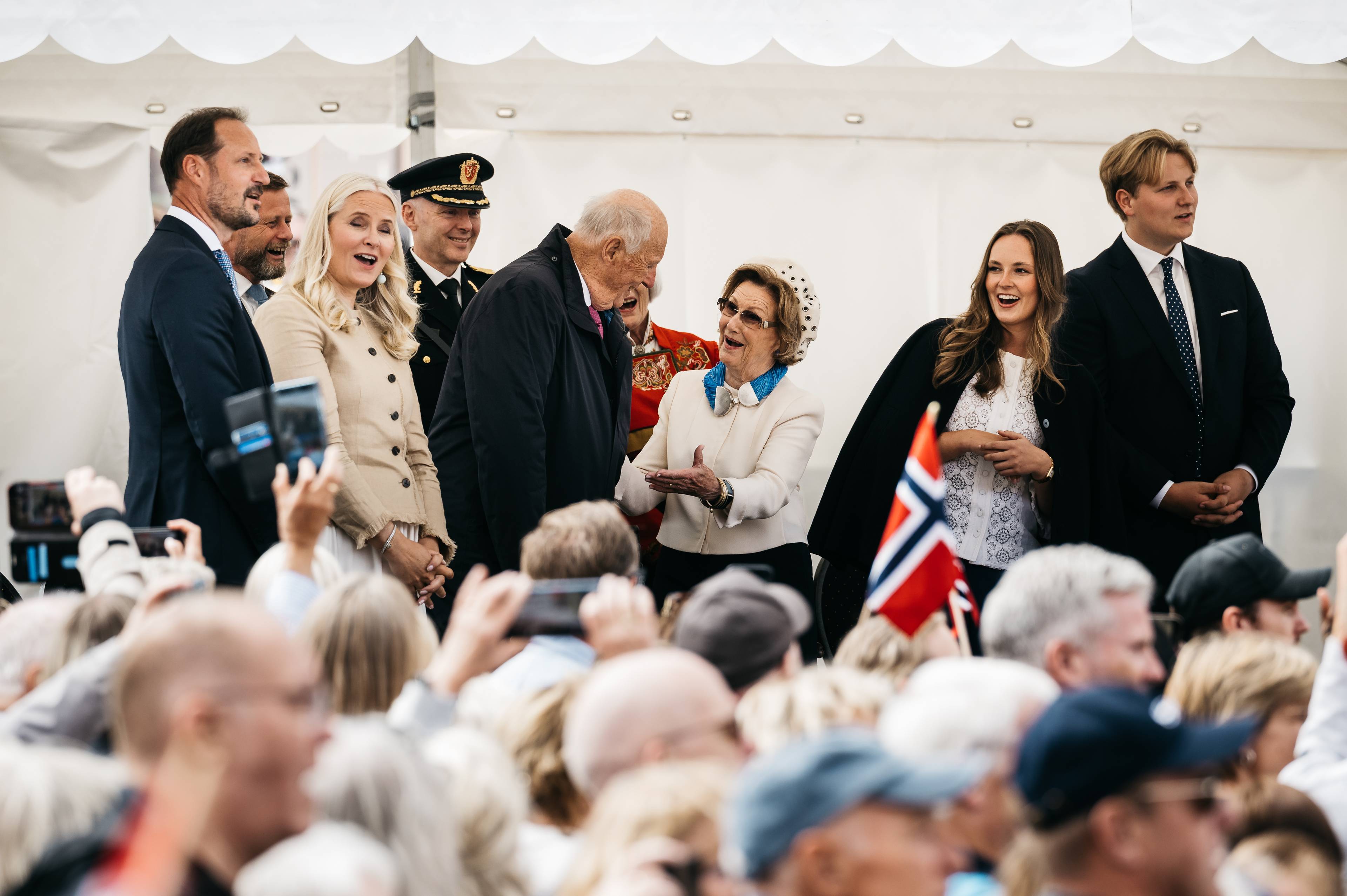 Dronning Sonja snur seg mot kong Harald når både kongefamilien og folk synger bursdagssangen for dronningen under kongefamiliens besøk i Stavanger i juli 2025.