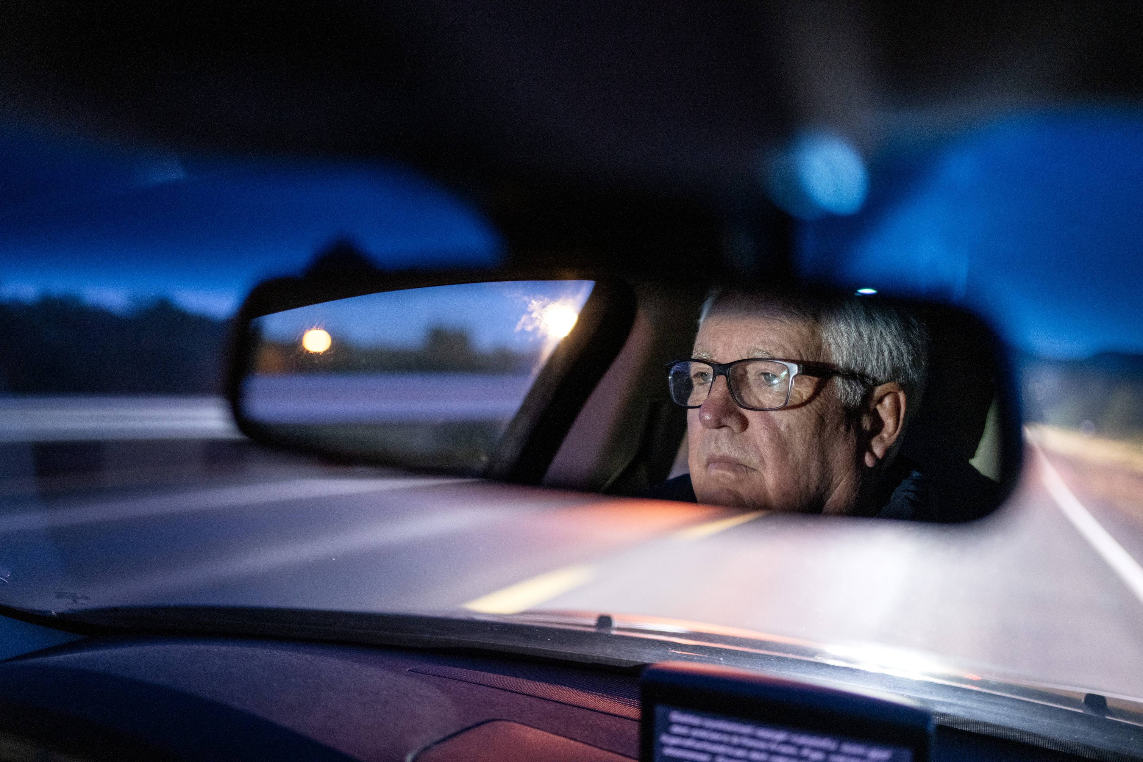 Erik Arntzen kjører bil og ansiktet hans er reflektert i frontspeilet. Det er mørkt utenfor og veien ser tom ut.
