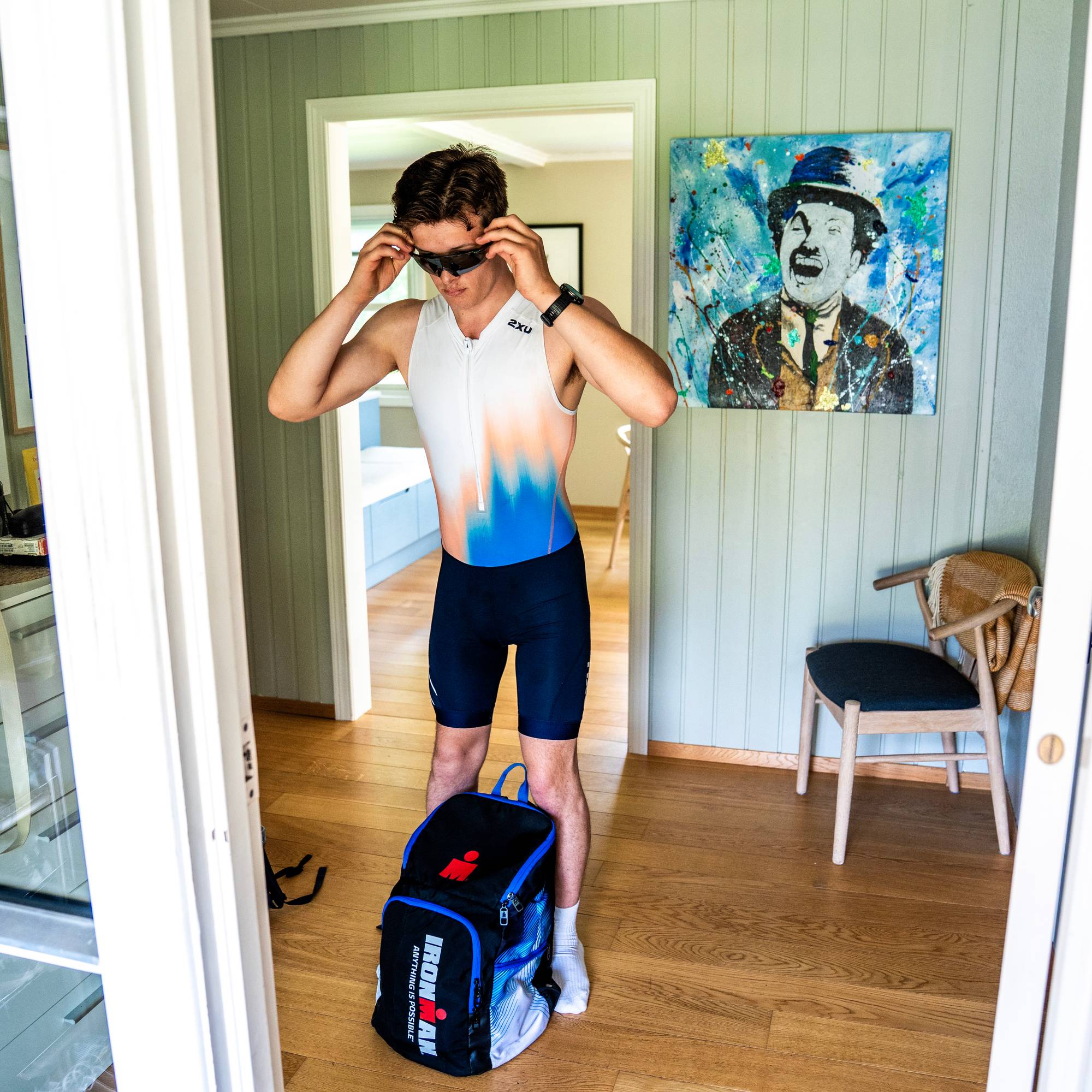 En mann med treningsdrakt står i gangen med en sekk foran og gjør seg klar til å gå ut.