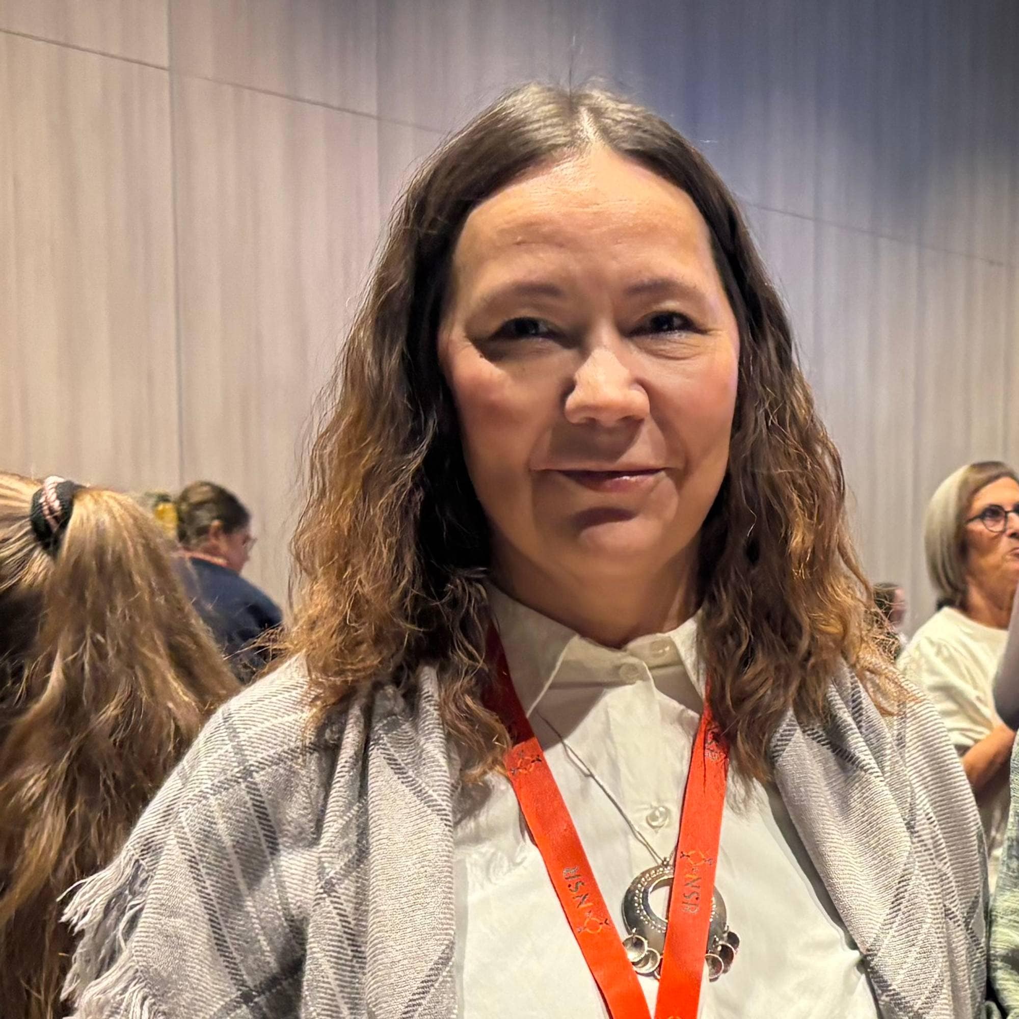 To kvinner står sammen i et konferanserom med flere mennesker i bakgrunnen. (Bildebeskrivelsen er laget av en KI-tjeneste)