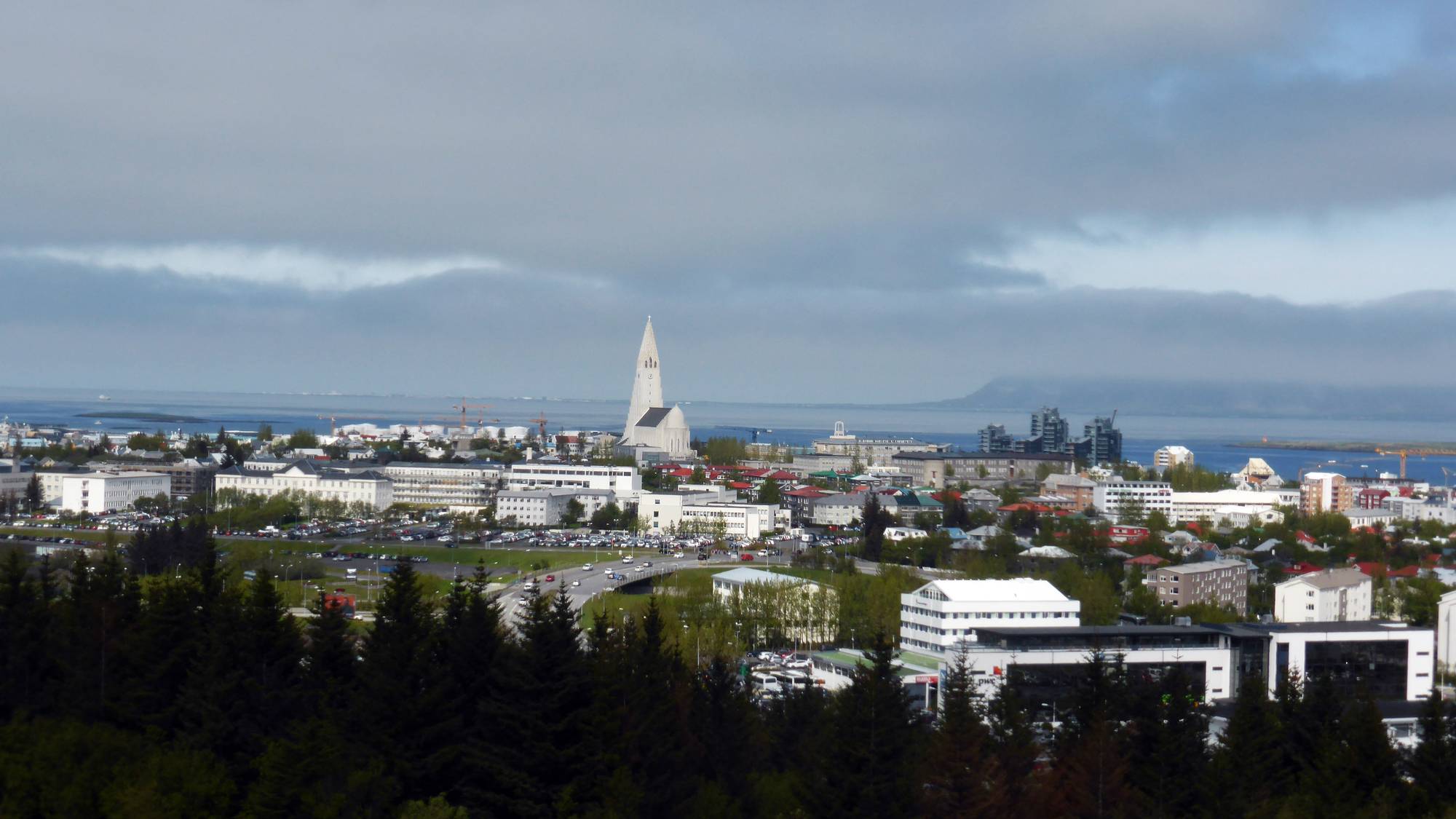 Utsikt over en by ved havet. En kirke med høyt tårn er synlig i bybildet. Tåke ligger over fjell i bakgrunnen. (Bildebeskrivelsen er laget av en KI-tjeneste)