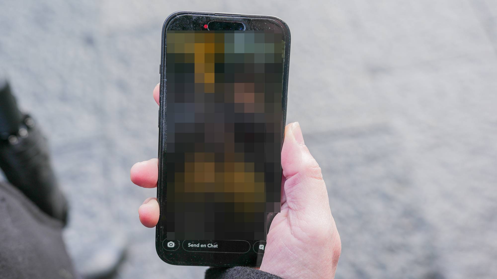 En hånd holder en smarttelefon med et bilde på skjermen som er sladdet. (Bildebeskrivelsen er laget av en KI-tjeneste)