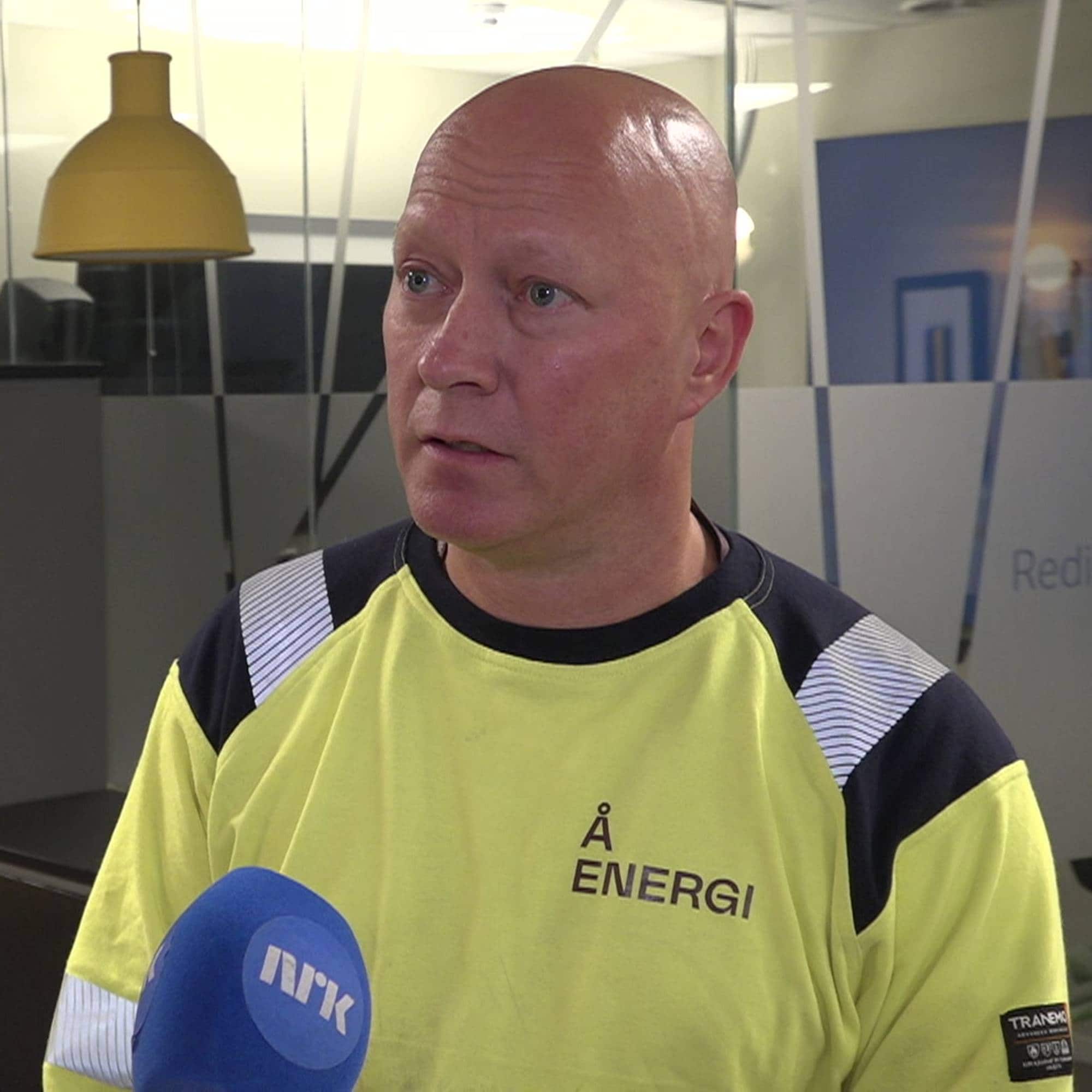 Mann i Å Energi-arbeidsklær blir intervjuet av NRK i et kontorlandskap. (Bildebeskrivelsen er laget av en KI-tjeneste)
