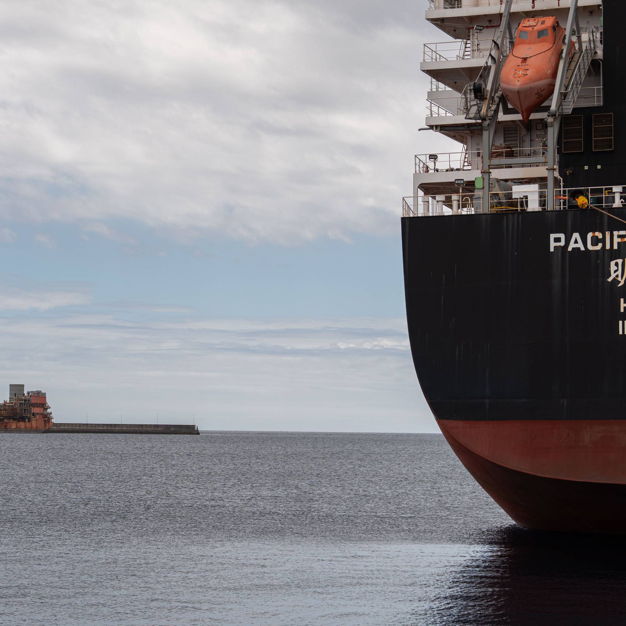 Et stort lasteskip ved navn "PACIFIC PROSPER" med opprinnelse i Hong Kong ligger ved kai. I bakgrunnen sees et annet, eldre skip. Begge fartøyene er til havs med en grå himmel. (Bildebeskrivelsen er laget av en KI-tjeneste)