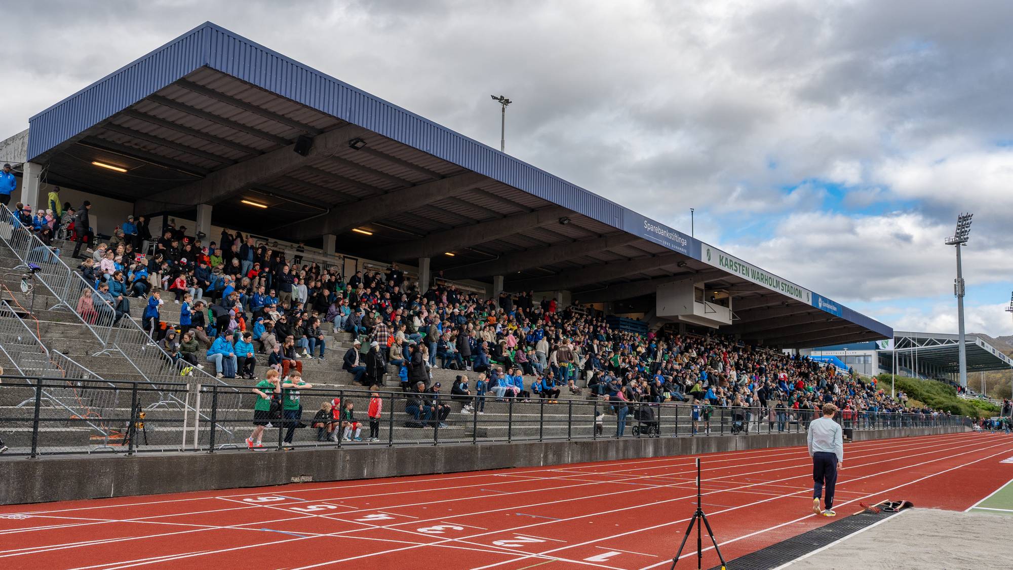 Publikum sitter på tribunen på Karsten Warholm stadion med røde løpebaner i forgrunnen. (Bildebeskrivelsen er laget av en KI-tjeneste)
