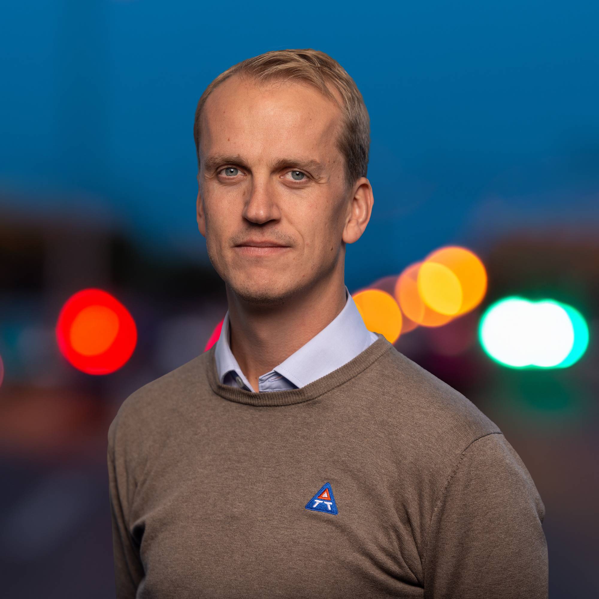 Knut Olav Røssland Nestås, regionsleder i Trygg Trafikk Vestland, med en brun genser og blå skjorte under. I bakgrunn ser man lys fra det som kan være trafikk. 
