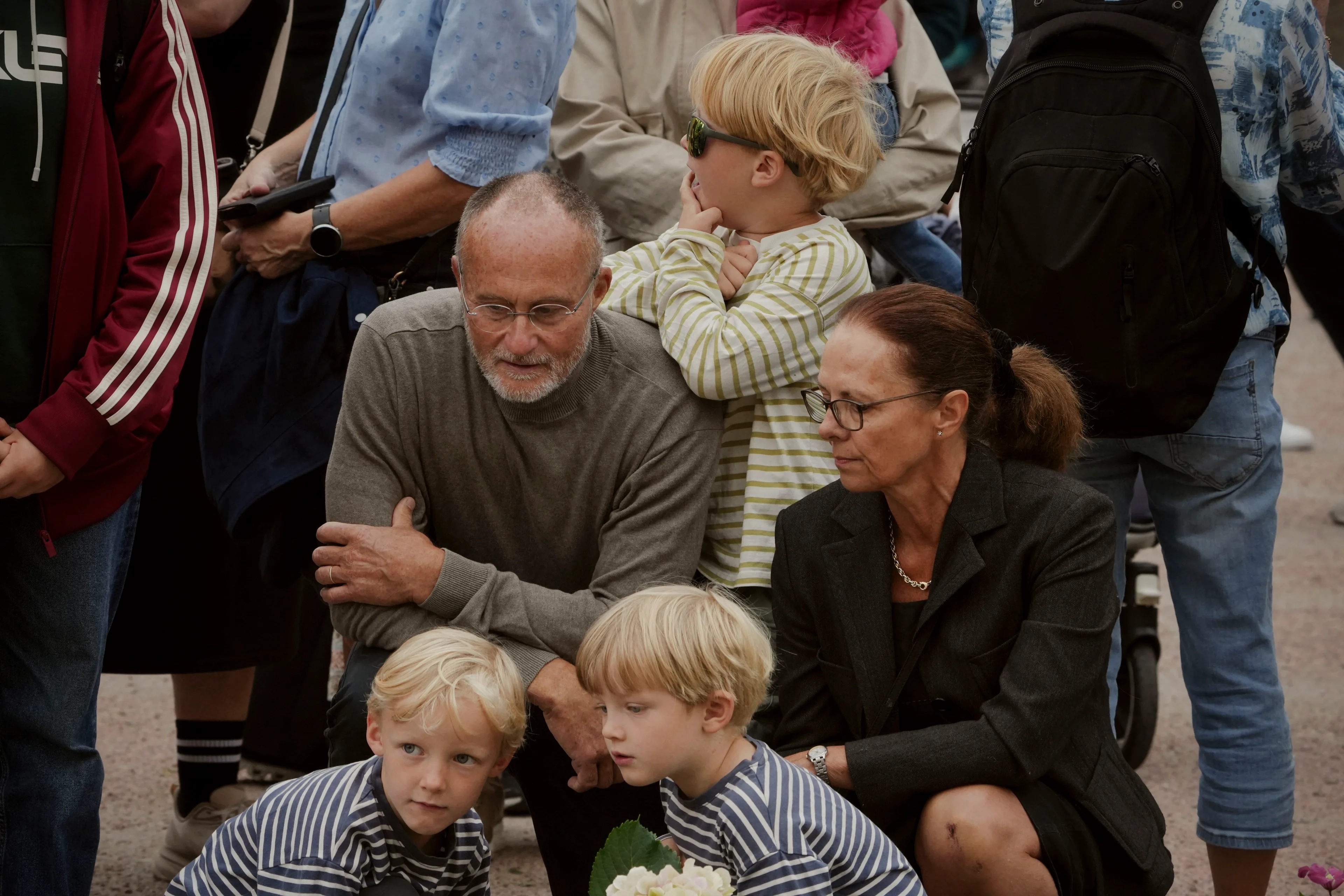 En eldre mann og kvinne sitter sammen med tre barn ute blant folk. (Bildebeskrivelsen er laget av en KI-tjeneste)