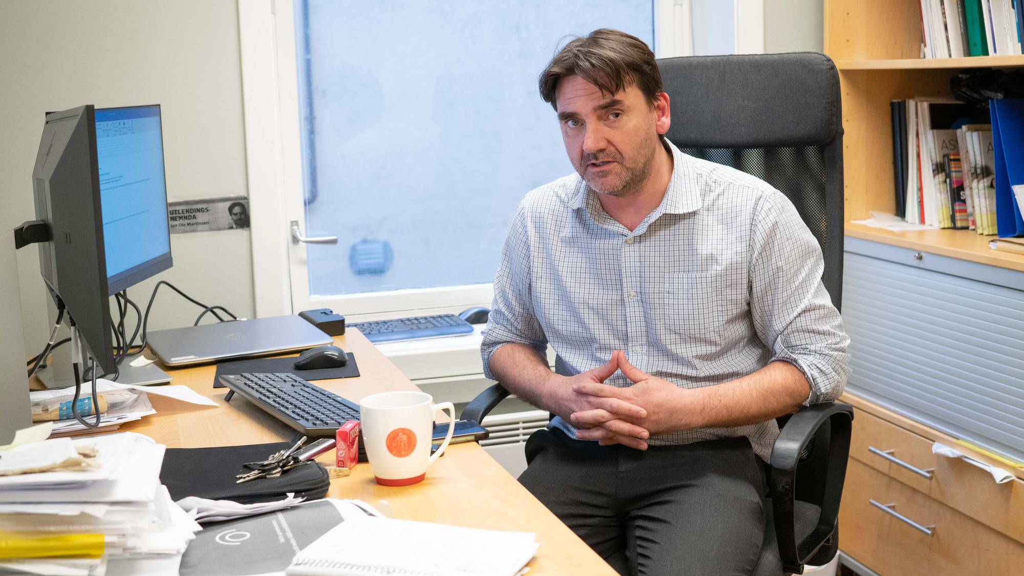 Jon Ole Martinsen, talsperson NOAS, sitter på et kontor, og på en kontorstol. Mannen folder hendene sine, og ser rett i kamera. Foran han er en pult med mye greier, og en pc. 