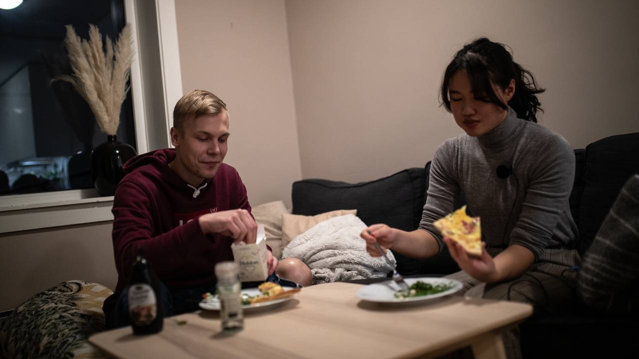 William og Tram sitter ved stuebordet og spiser pizza i sofaen i kollektivet.