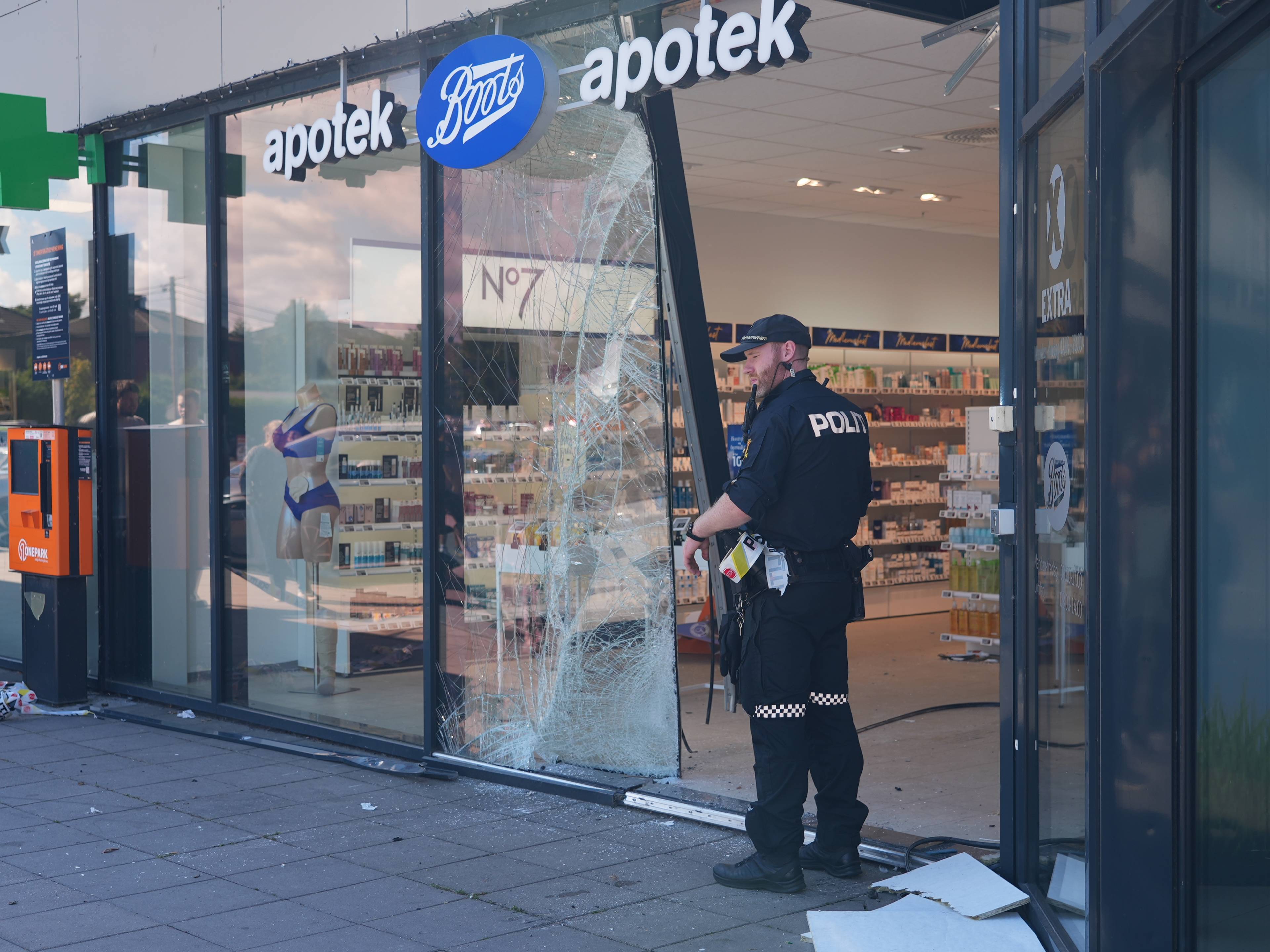 Politibetjent undersøker knust glassrute ved et Boots apotek. (Bildebeskrivelsen er laget av en KI-tjeneste)