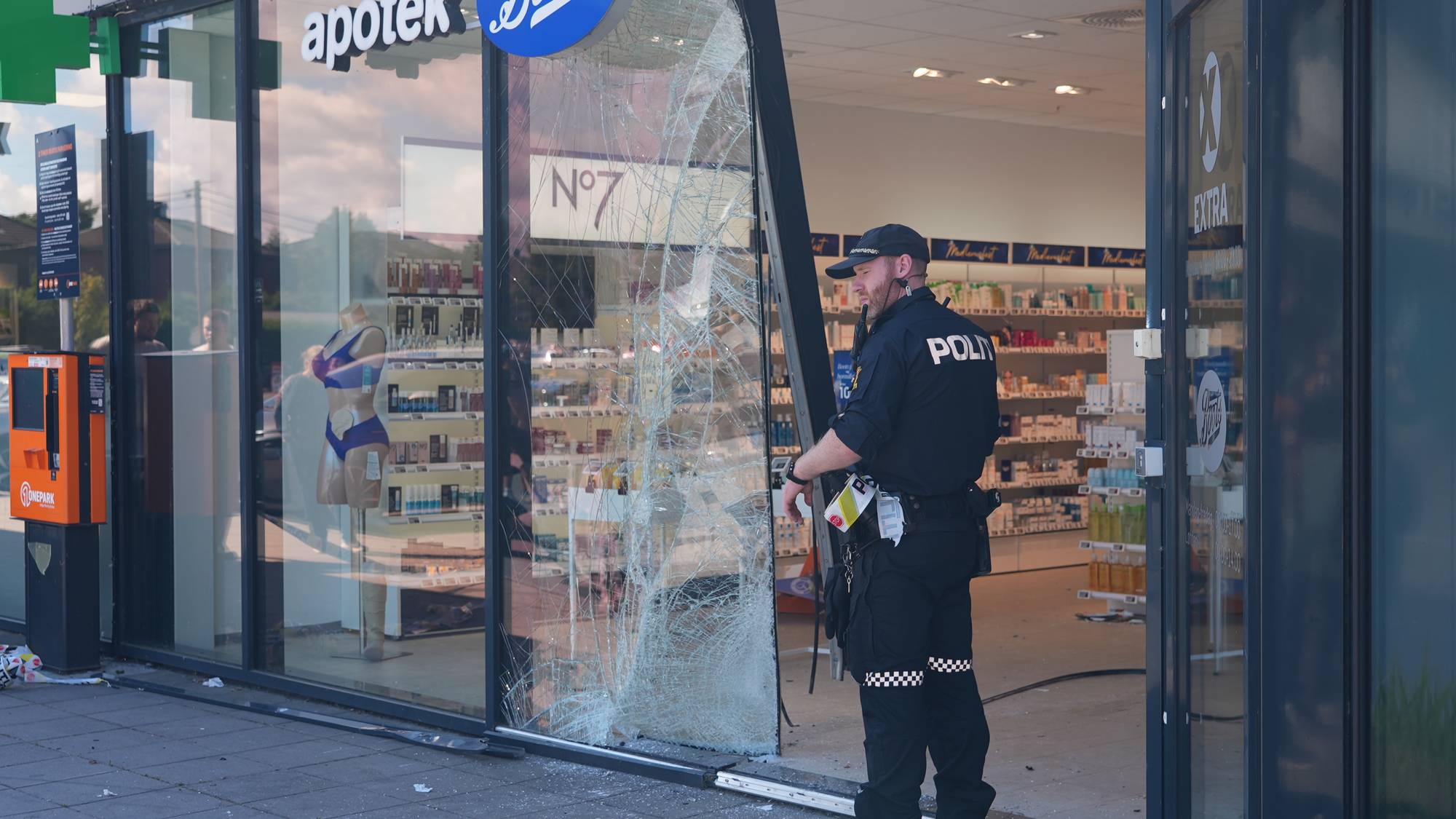 Politibetjent undersøker knust glassrute ved et Boots apotek. (Bildebeskrivelsen er laget av en KI-tjeneste)