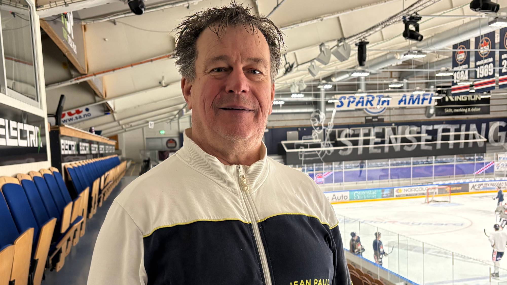 Mann med hvit genser står inne i en ishockeyhall