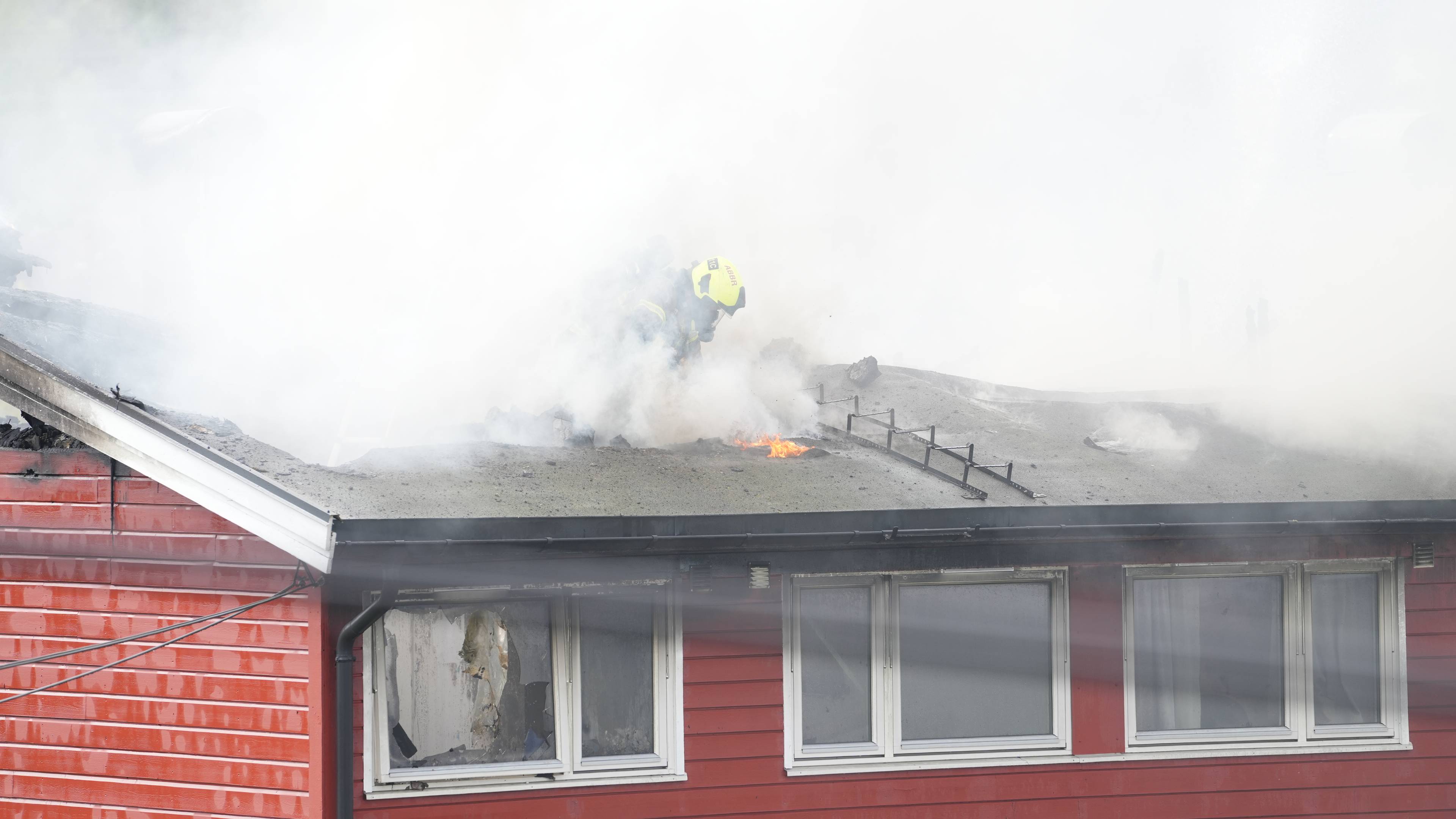 En brannmann går ned en stige inn i taket på det brennende rekkehuset
