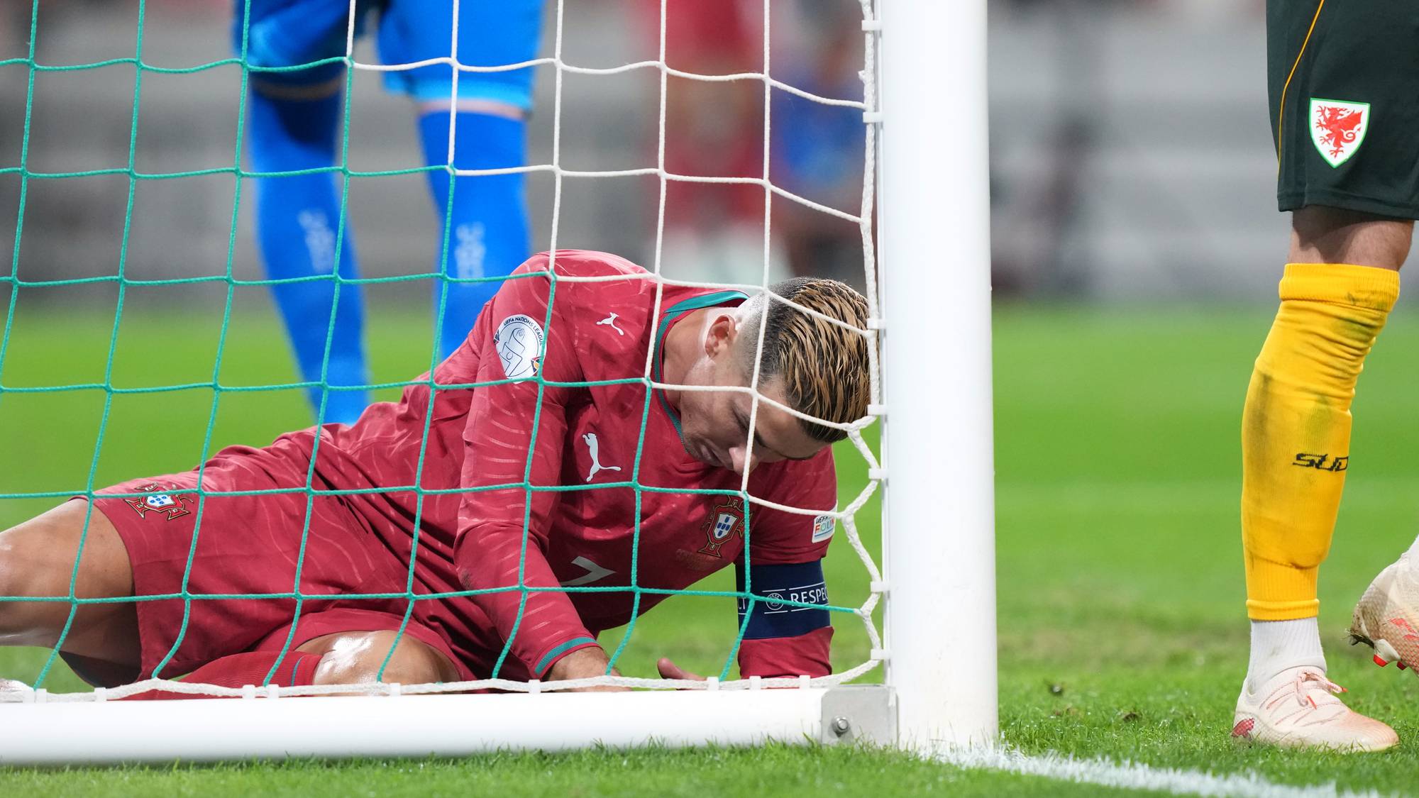 Fotballspiller i rød drakt ligger på bakken ved siden av et fotballmål etter en kamp. (Bildebeskrivelsen er laget av en KI-tjeneste)
