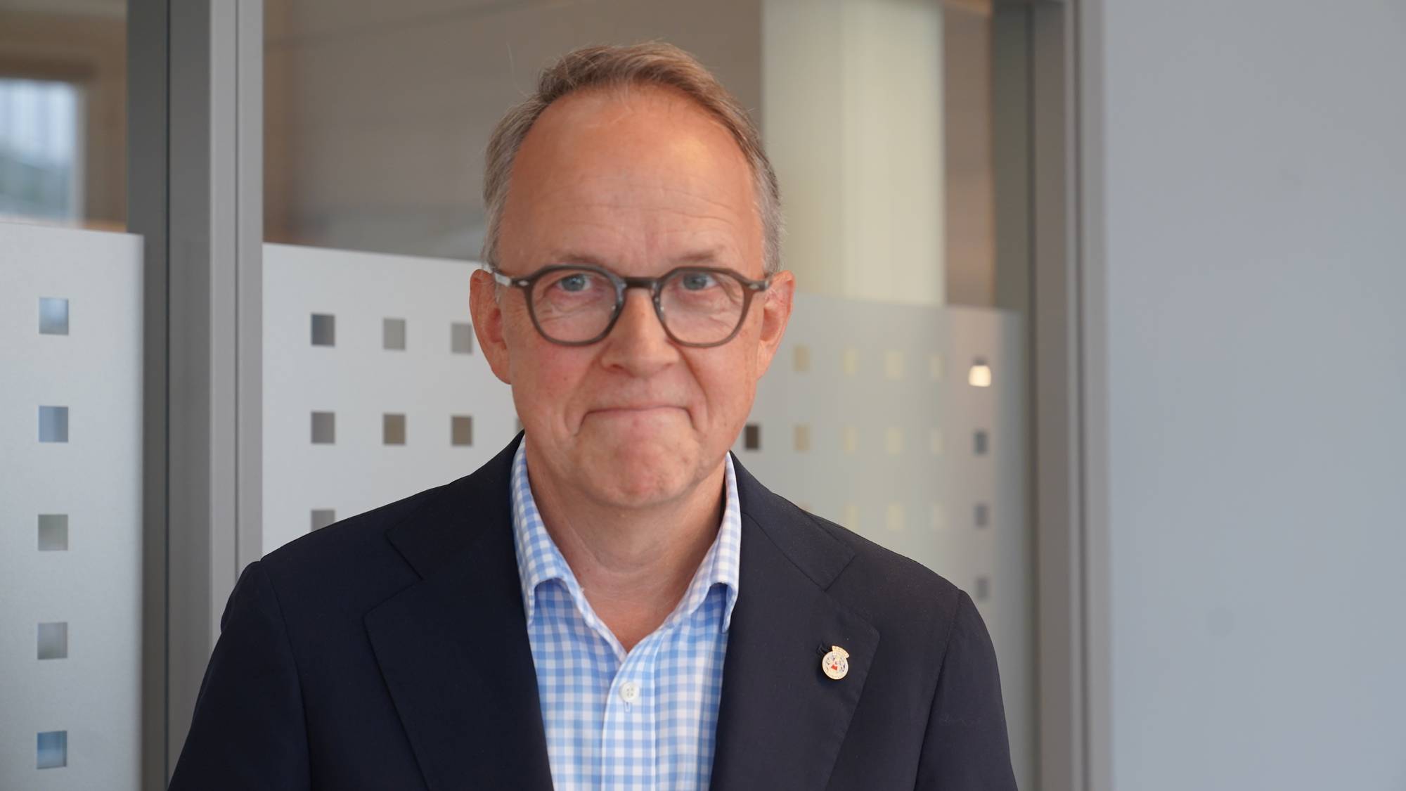 Mann med kort hår og brille, i blå blazer smiler til kamera