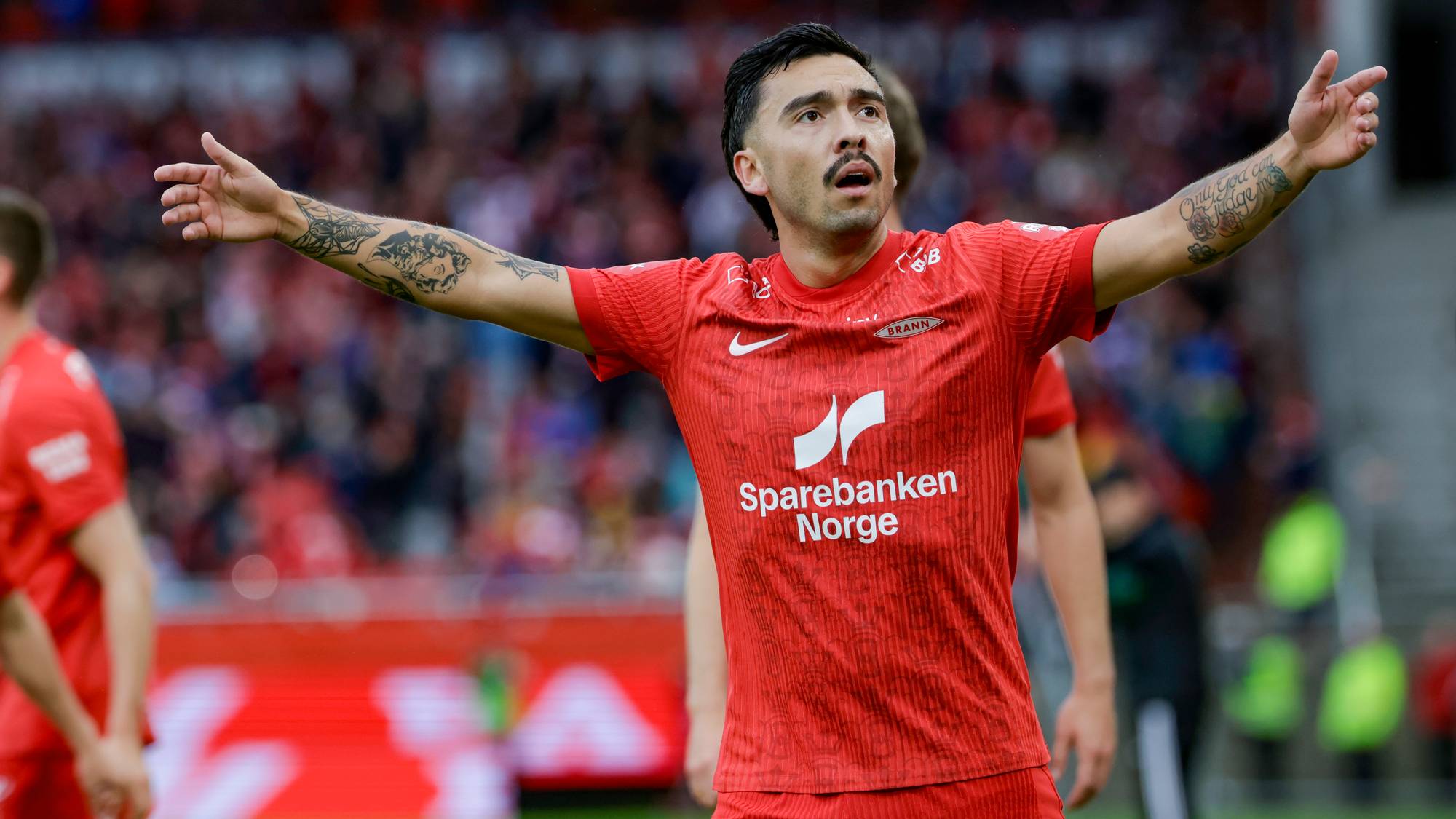 Fotballspiller fra Brann feirer med armene utstrakt på en fotballstadion. (Bildebeskrivelsen er laget av en KI-tjeneste)
