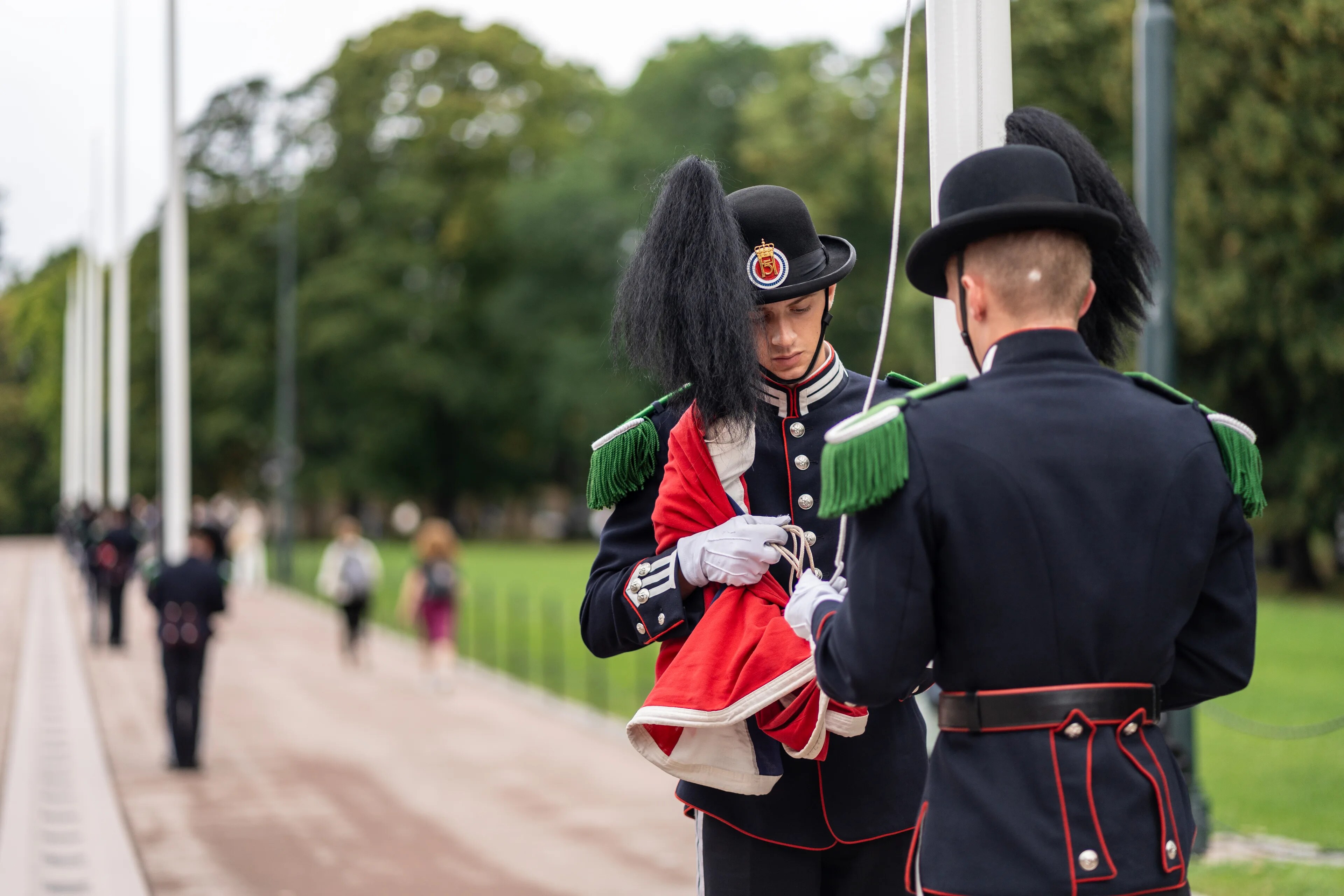 To gardistar i uniform heiser flagget ved Det kongelege slott i Oslo. (Bildebeskrivelsen er laget av ein KI-teneste)