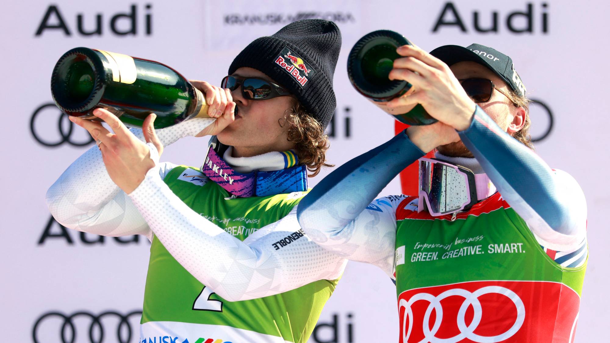 To utøvere i skiklær feirer med champagne på pallen foran en Audi-sponsorvegg. (Bildebeskrivelsen er laget av en KI-tjeneste)