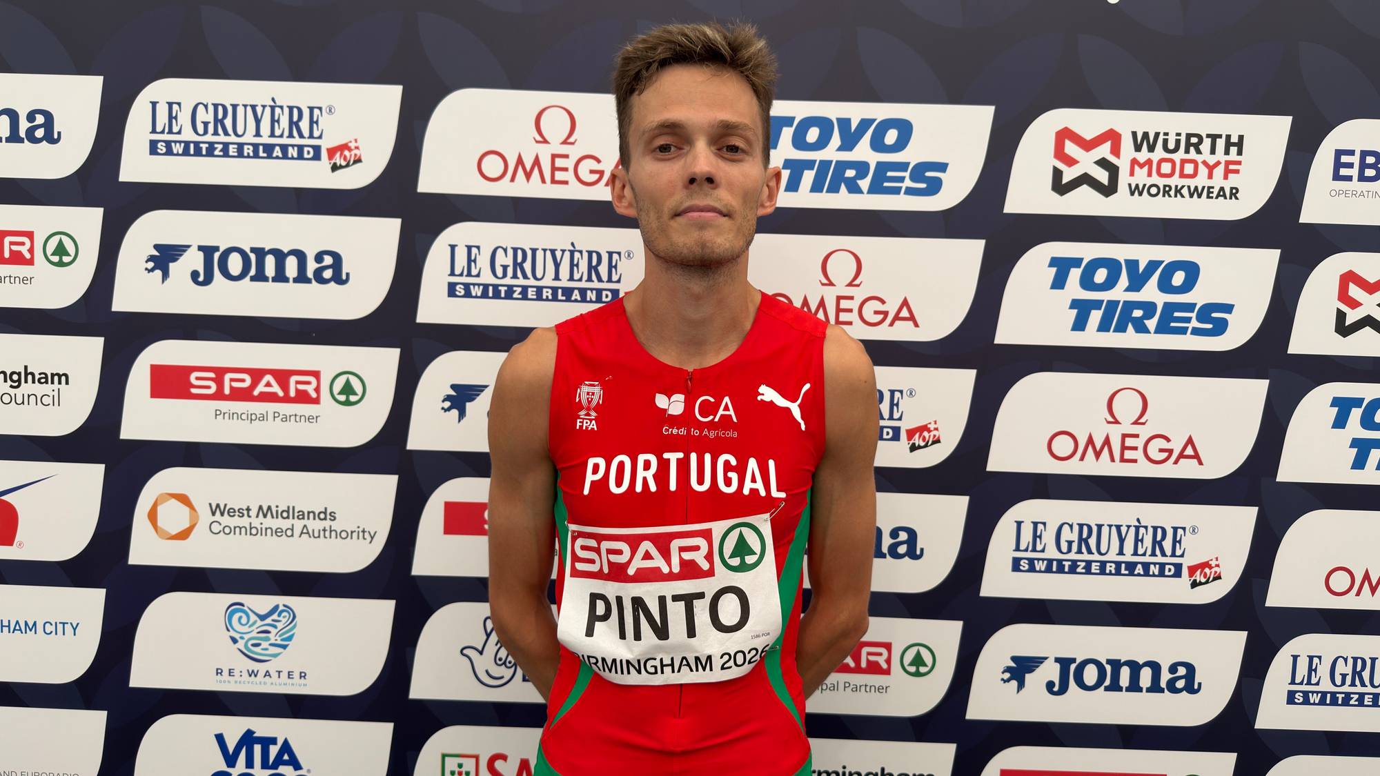En mann i løpesinglet foran en sponsorvegg.