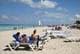 Norlys Perez / REUTERS,NTB Folk ligger på solsenger på en strand med turkist vann. Flere båter med seil er synlige på havet. Enkelte går langs vannkanten, mens andre sitter eller ligger på solsenger. (Bildebeskrivelsen er laget av en KI-tjeneste)