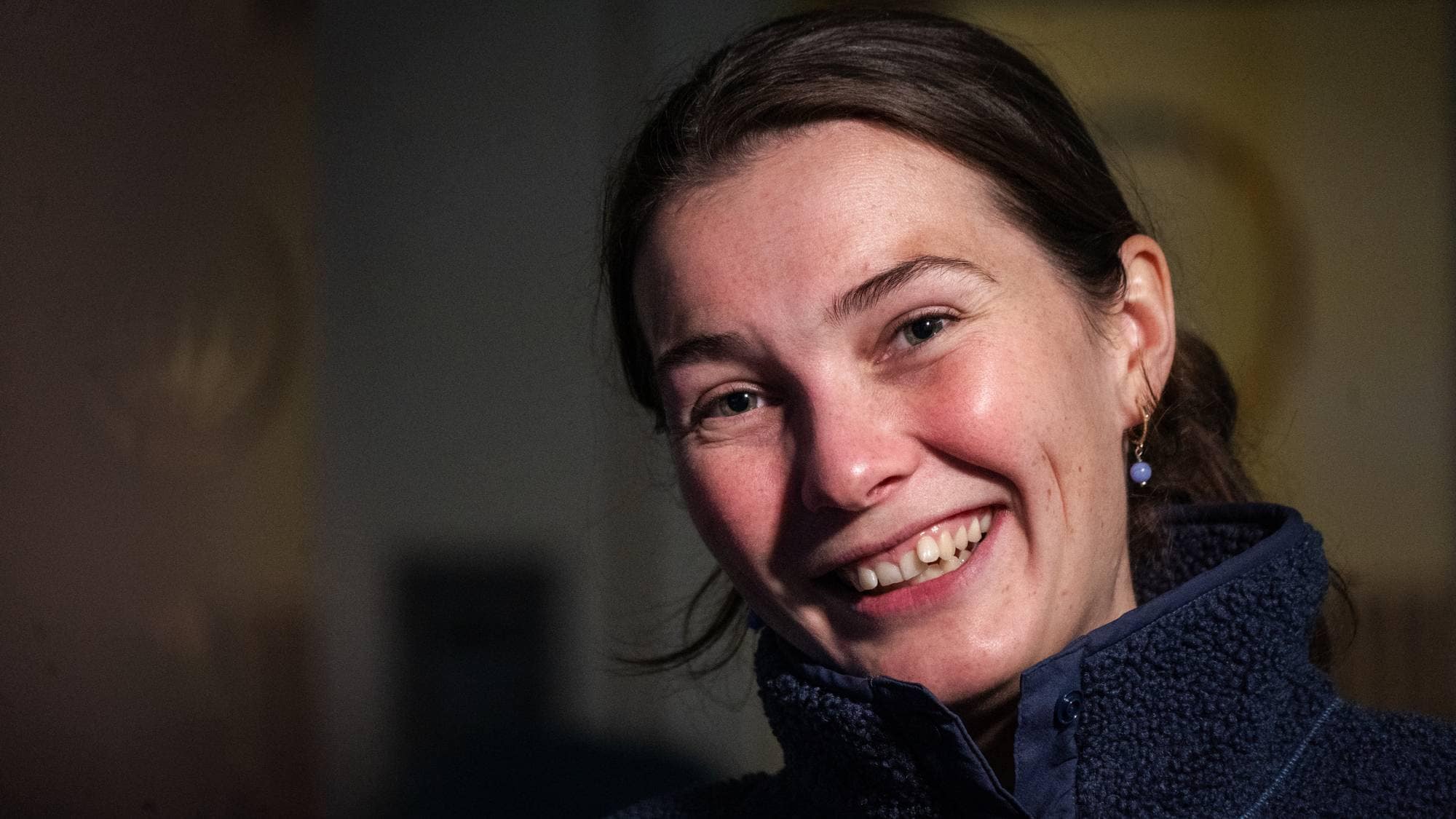 Portrett av en smilende kvinne i en mørkeblå fleecegenser. (Bildebeskrivelsen er laget av en KI-tjeneste)