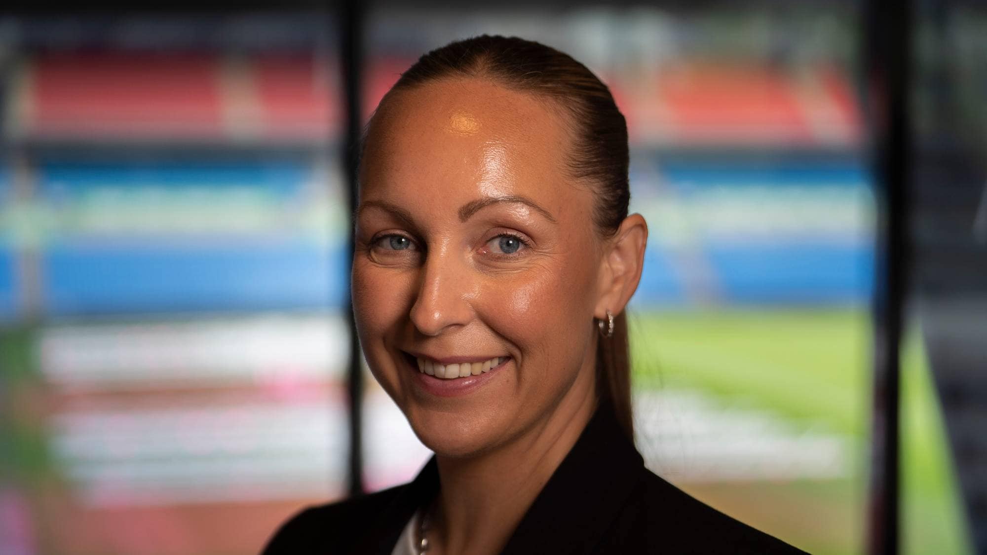 En kvinne smiler i kamera, vi ser konturene av en stadion i bakgrunnen.
