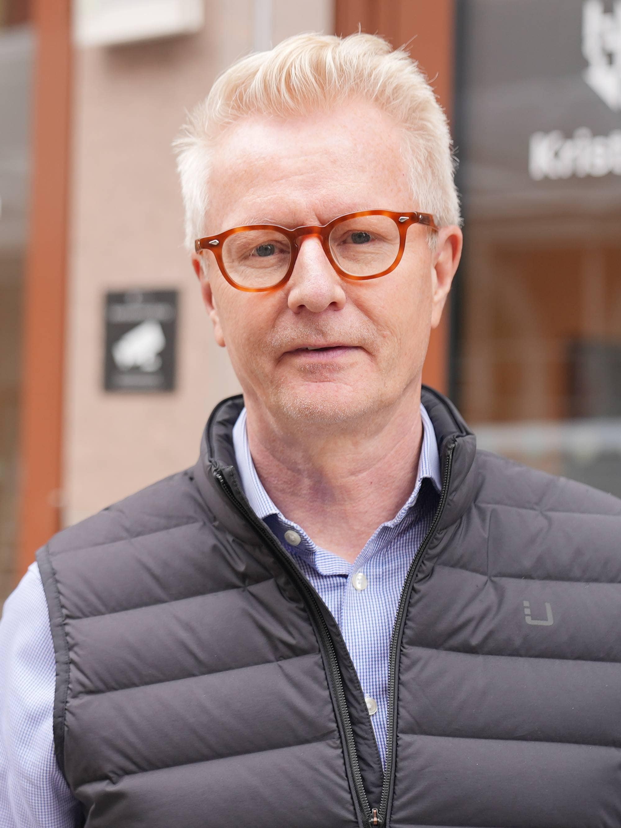 Mann med kort hår og boblevest står føre Høgskolen Kristiania.
