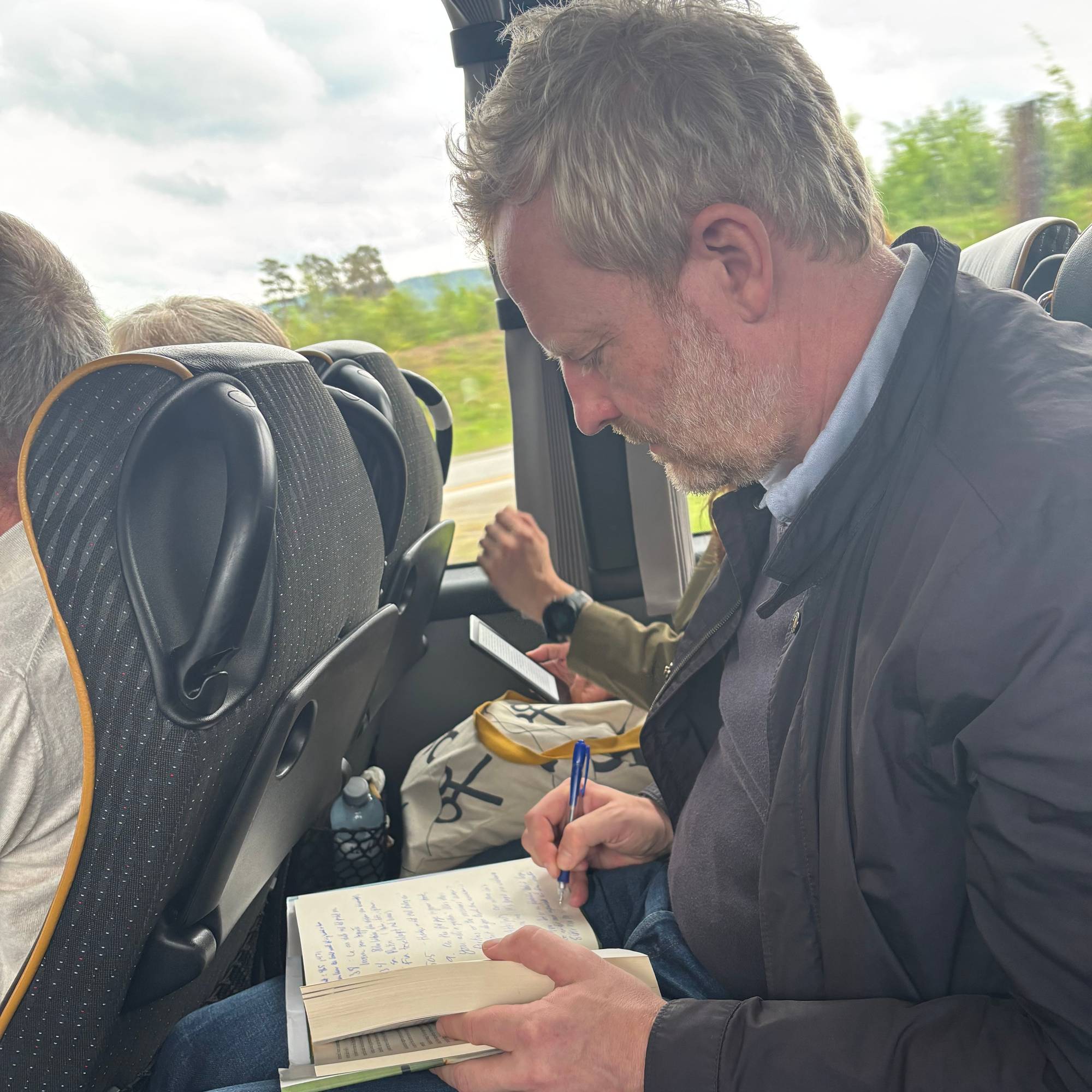 en mann i en fullsatt buss som tar notater i en tjukk bok