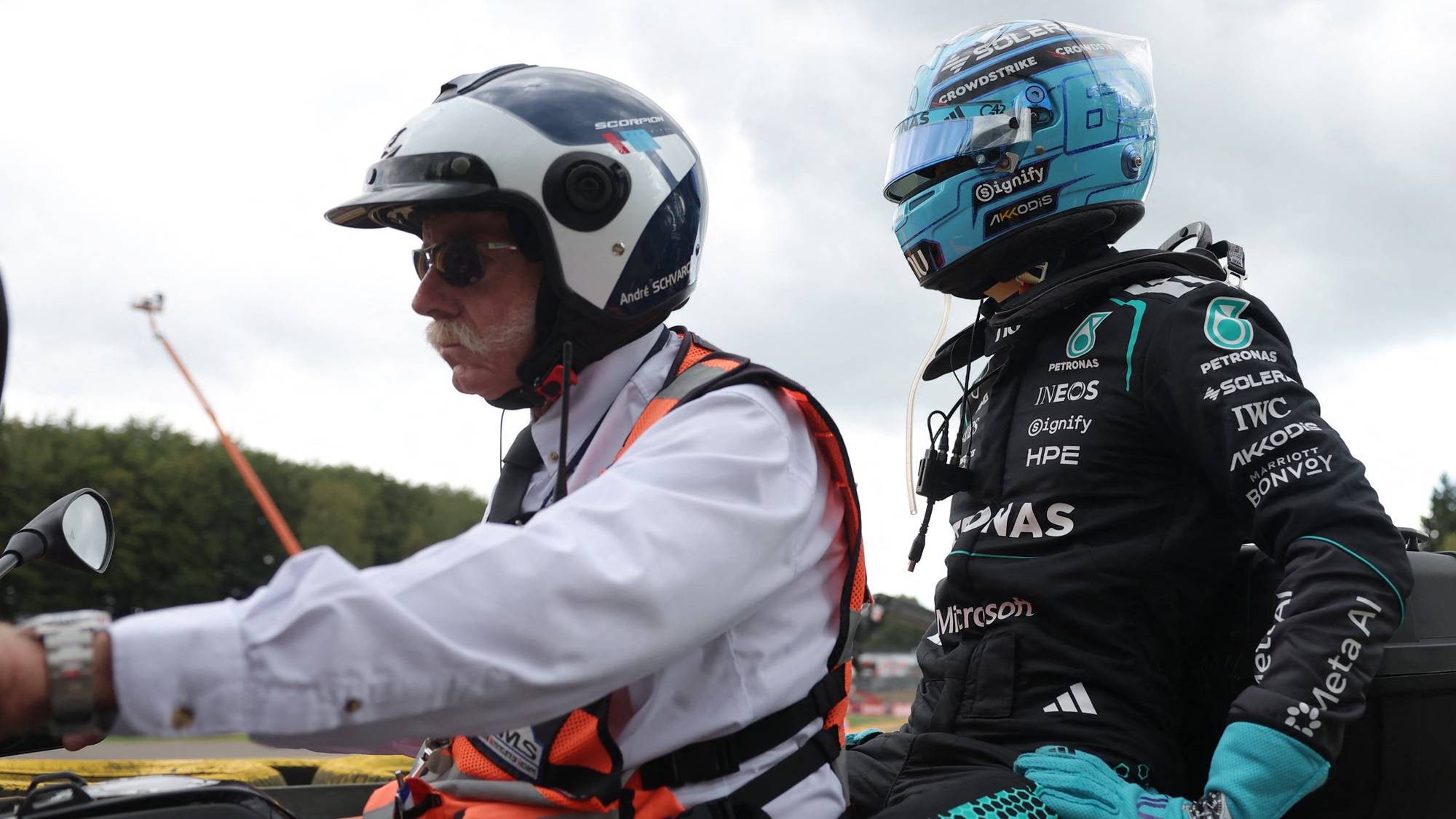 Formel 1-fører bakpå en motorsykkel med en funksjonær på en racerbane. (Bildebeskrivelsen er laget av en KI-tjeneste)