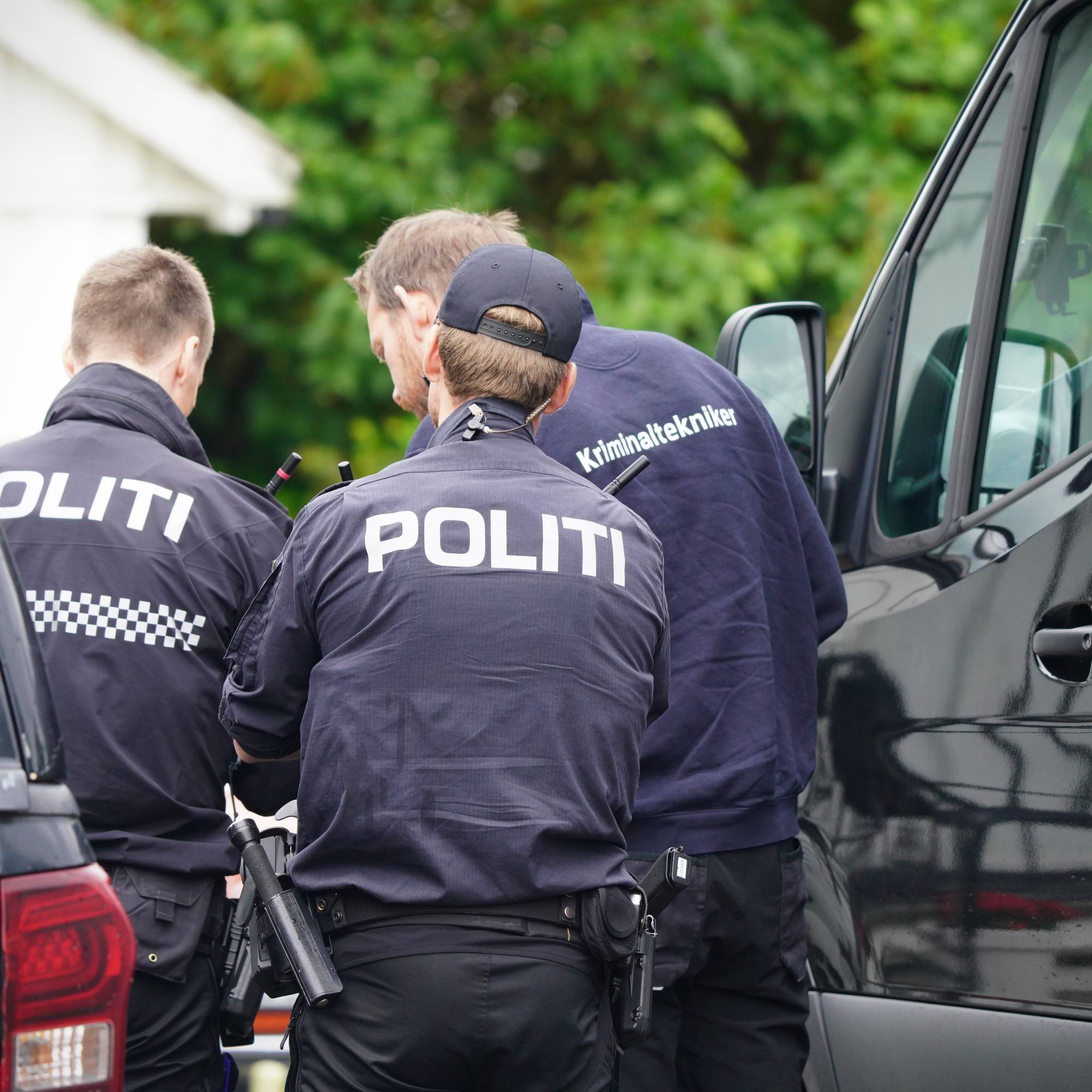 Tre politibetjenter i mørke uniformer står ved siden av en svart varebil. På ryggen av uniformene deres står det "POLITI" og på en av dem står det "Kriminaltekniker".