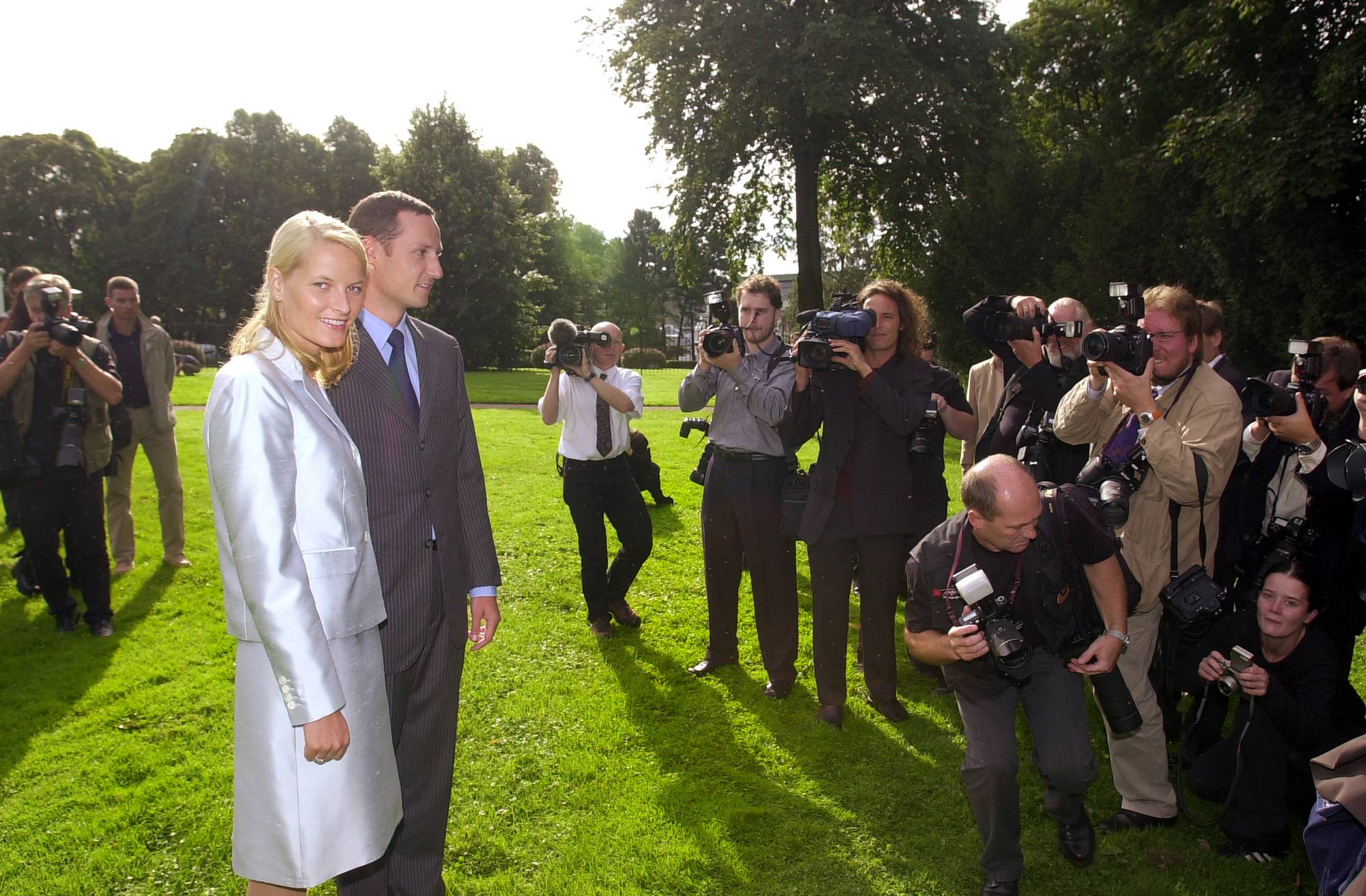 Kronprins Haakon og Mette-Marit Tjessem Høiby er omringet av fotografer i Slottsparken