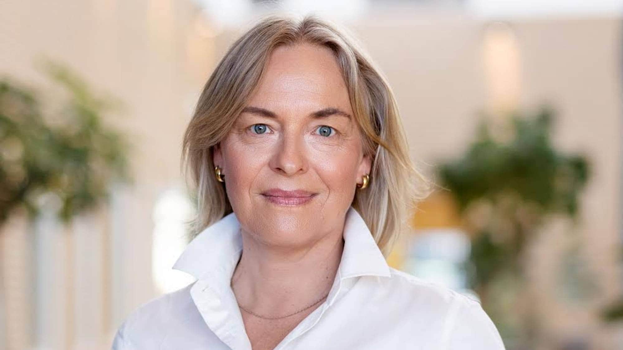 Kvinne i hvit skjorte smiler til kameraet. 