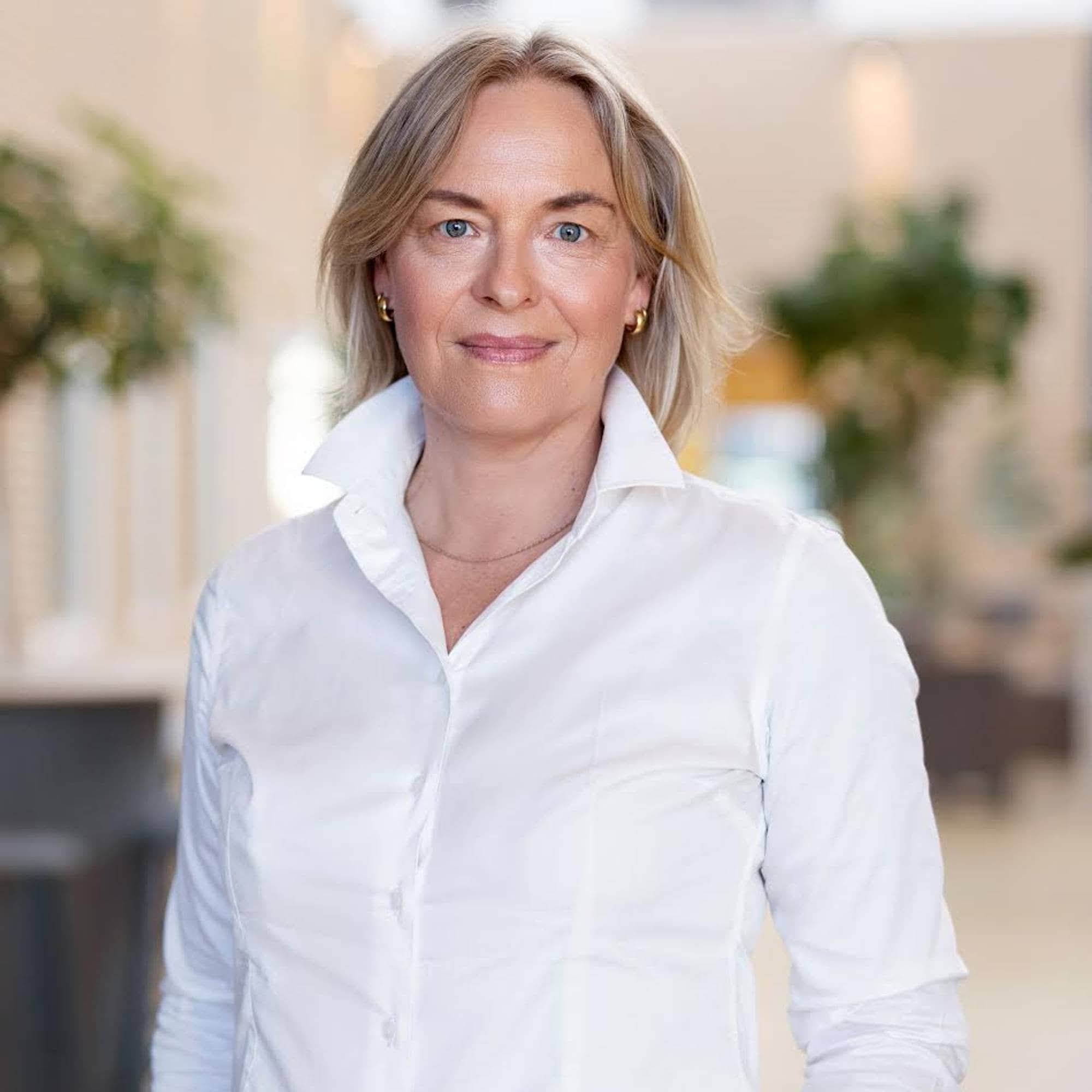 Kvinne i hvit skjorte smiler til kameraet. 