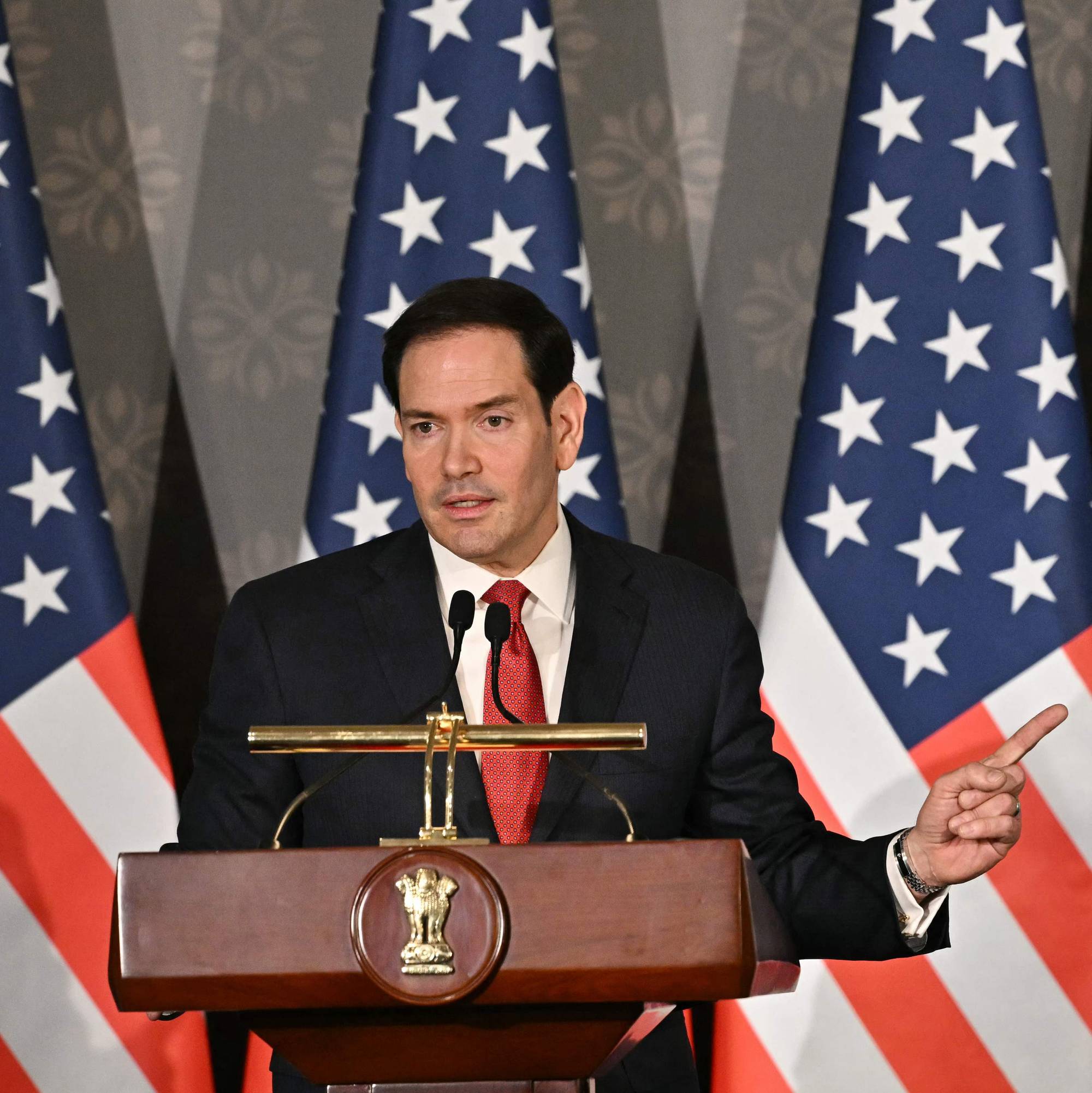 Marco Rubio på en talerstol med amerikanske flagg bak seg, holder opp en finger