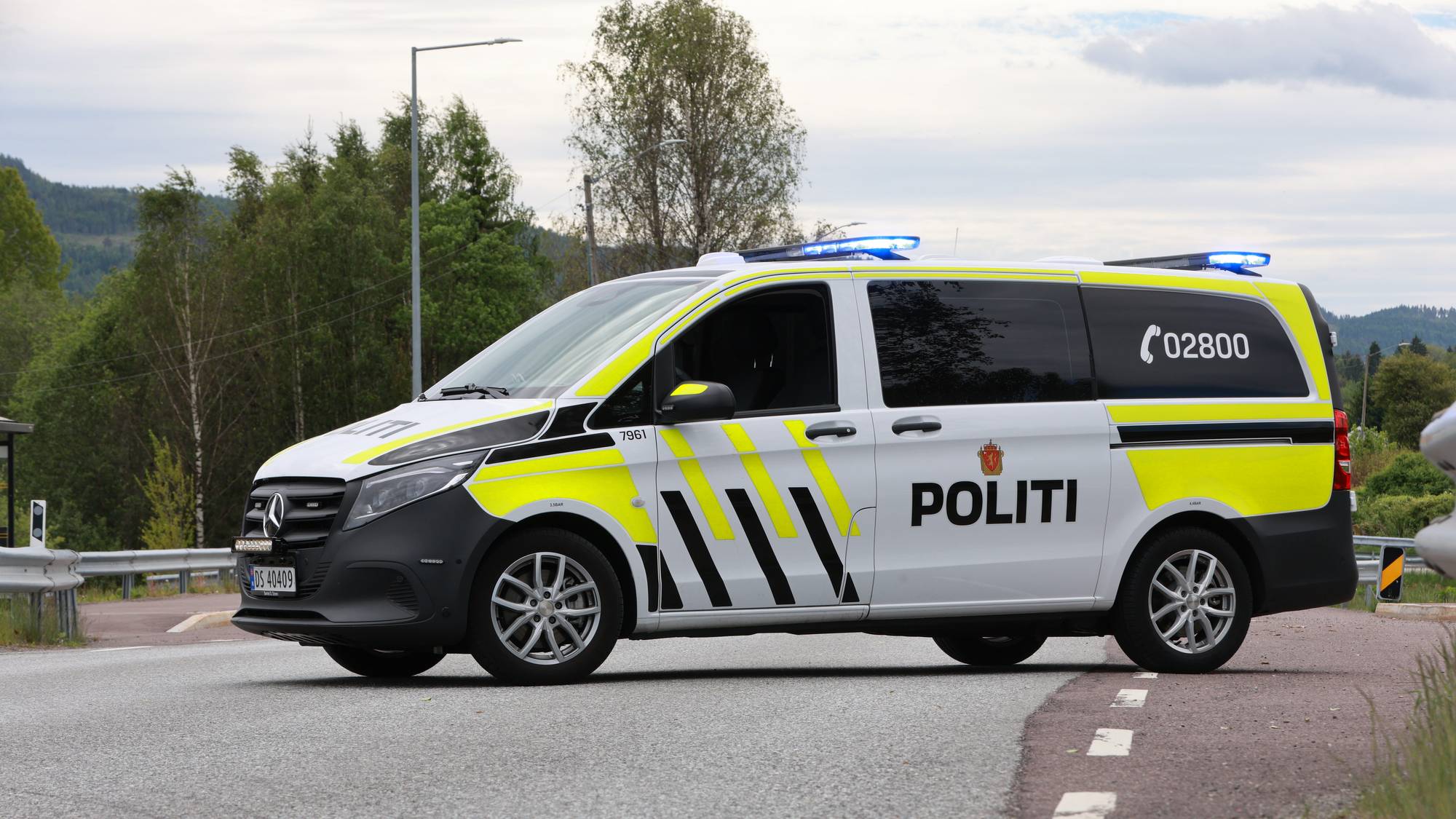 En politiesivilbil med blålys står på en landevei. Bilen er hvit med gule og svarte markeringer. 