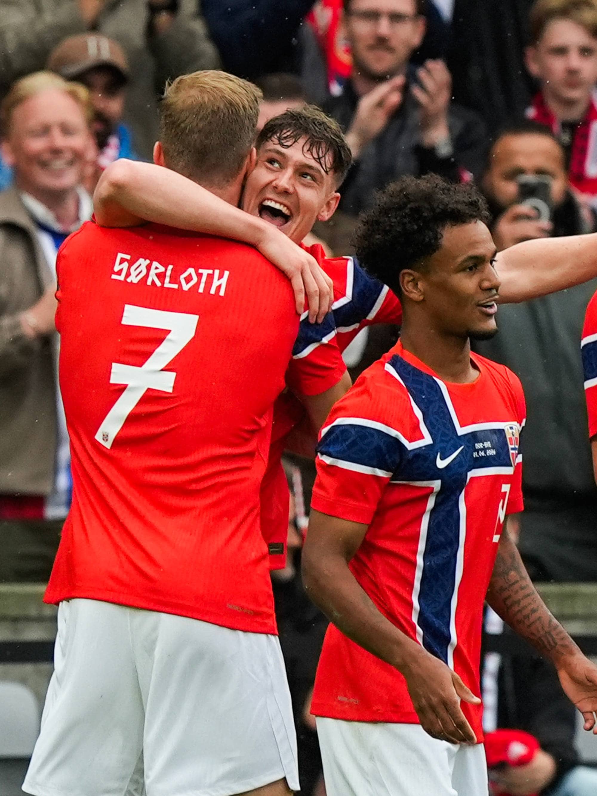 Fotballspillere i norske drakter feirer. En spiller med nummer 7 på ryggen blir gratulert av medspillere. Andre spillere og publikum ser på i bakgrunnen. (Bildebeskrivelsen er laget av en KI-tjeneste)