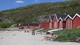 Katarina Trymsdatter Vatnvåg / NRK Bak ei lys strand er det ei rekke med røde naust. På stranda sit det to damer og soler seg.